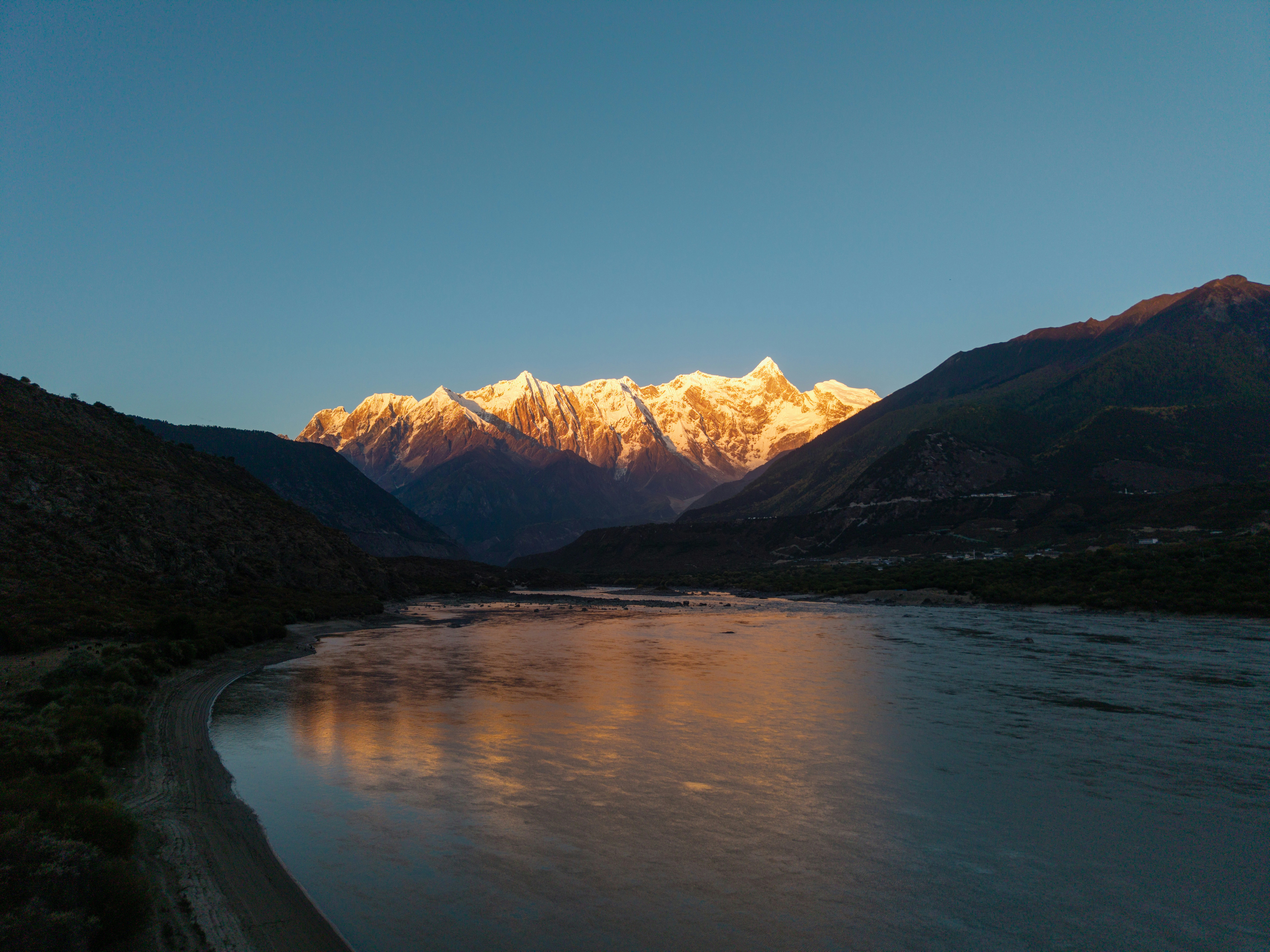 Golden mountain peaks illuminated by sunrise over a wide river.