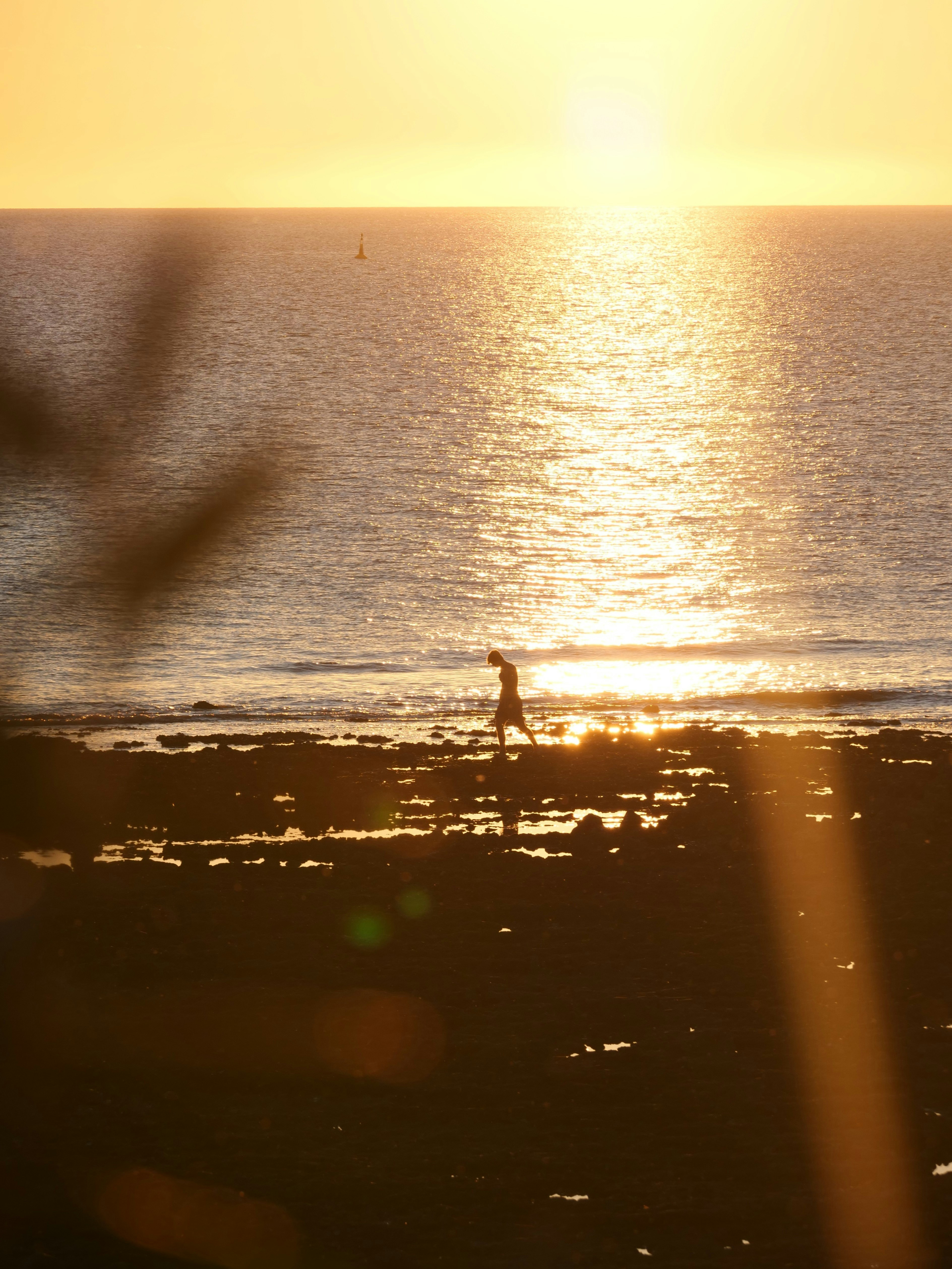 A lone figure walks along a rocky shore at sunset.