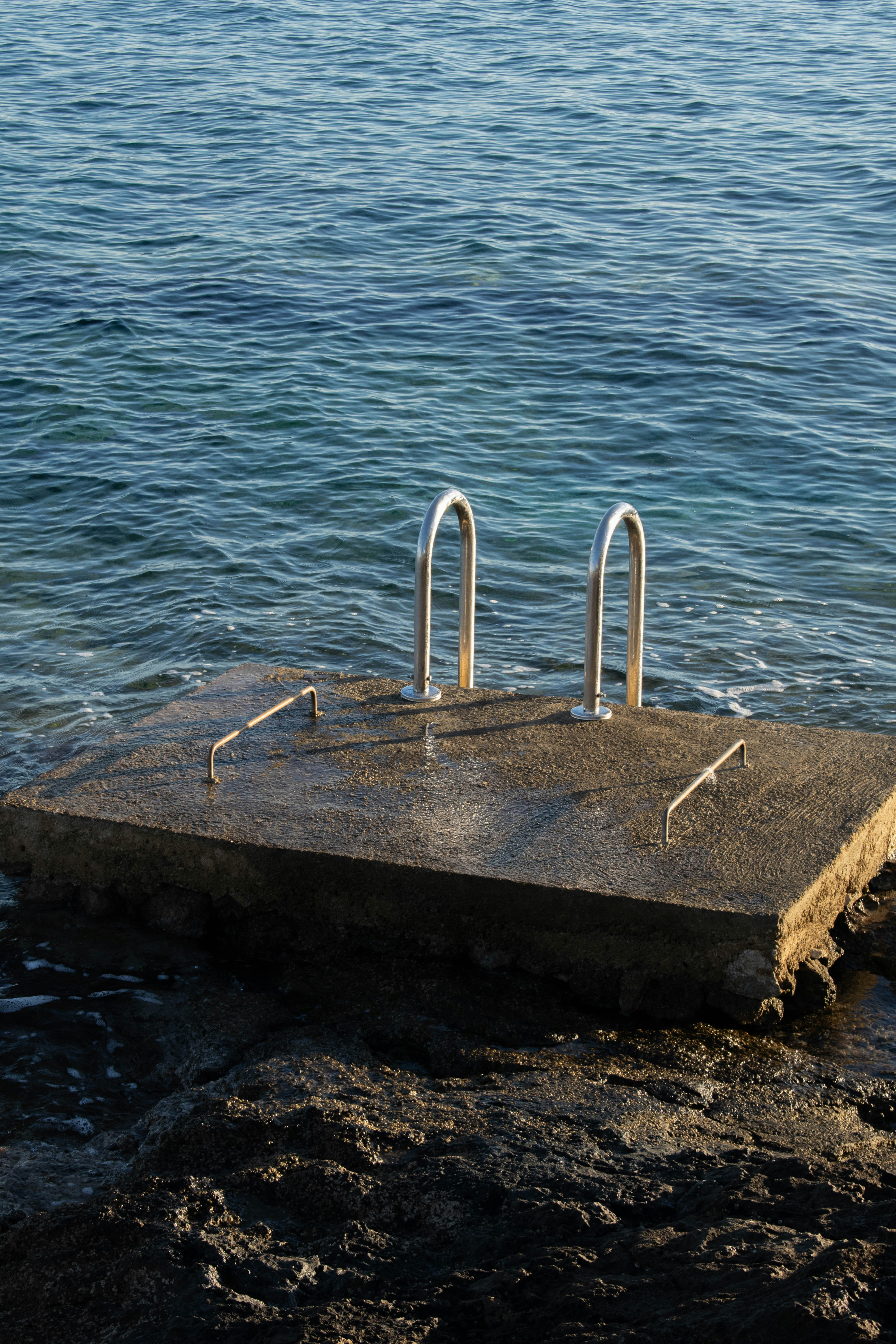 Concrete platform with metal ladder in calm ocean water photo – Free ...