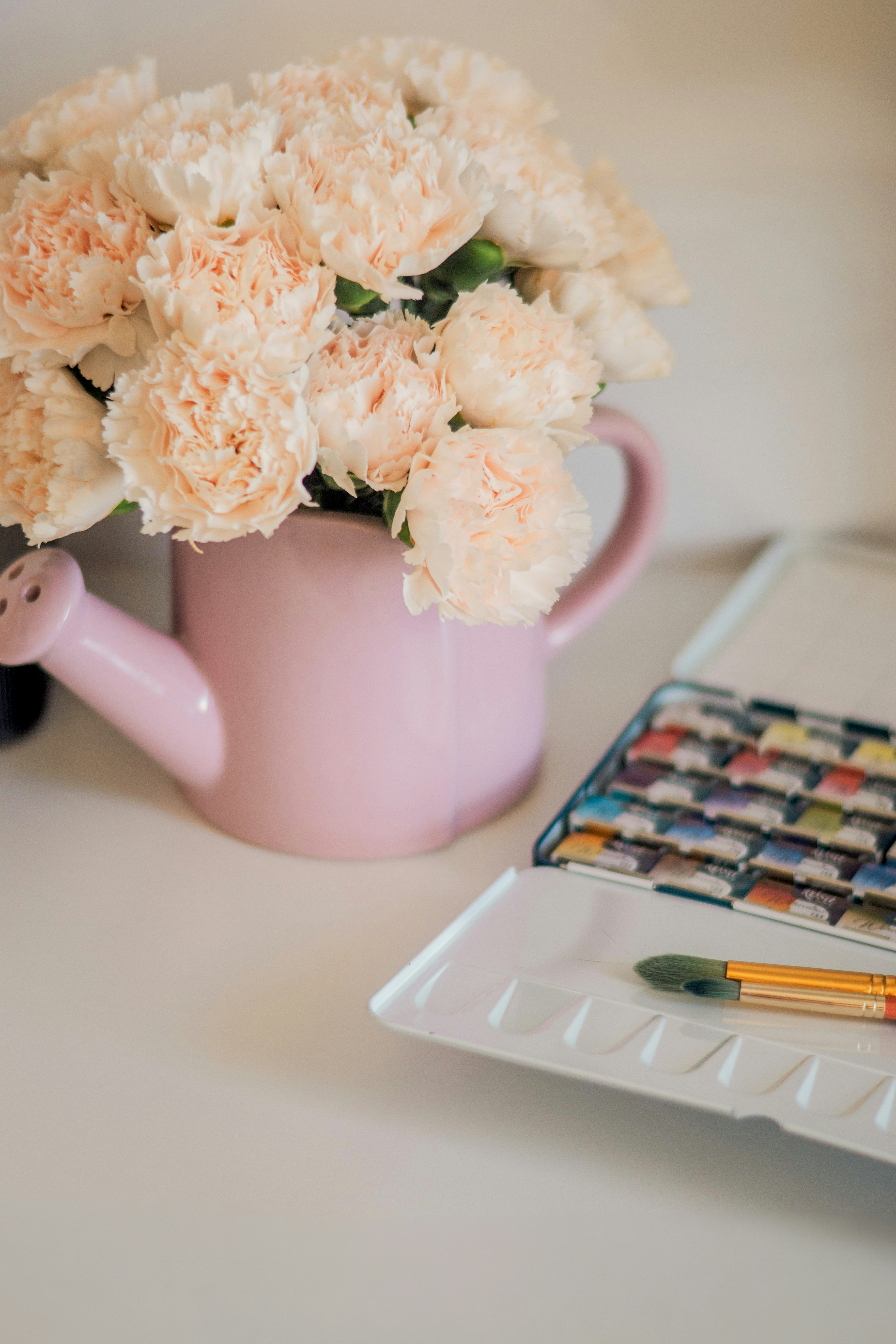 Pink watering can with pale flowers and watercolors