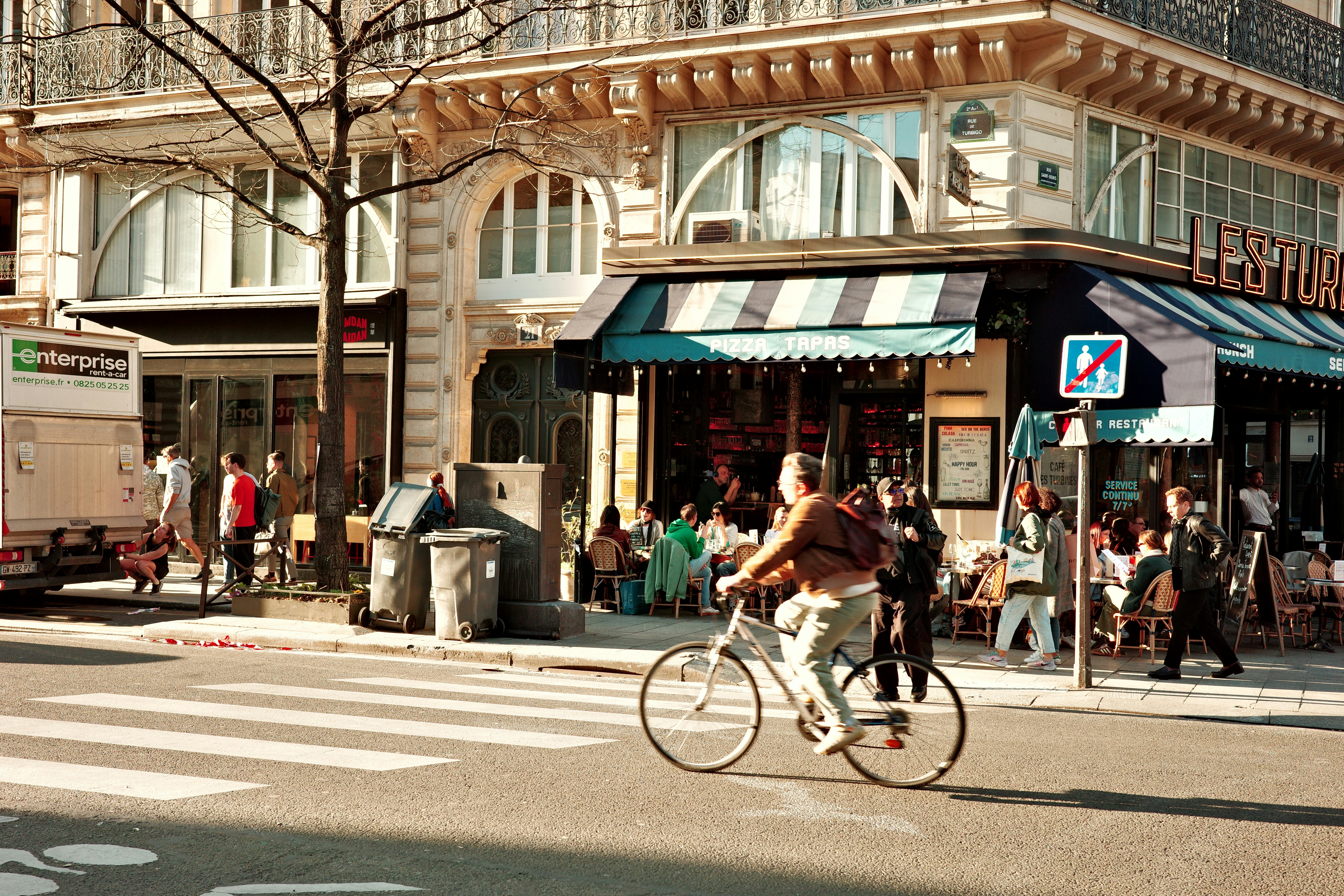 Man rides bicycle past outdoor cafe in paris.