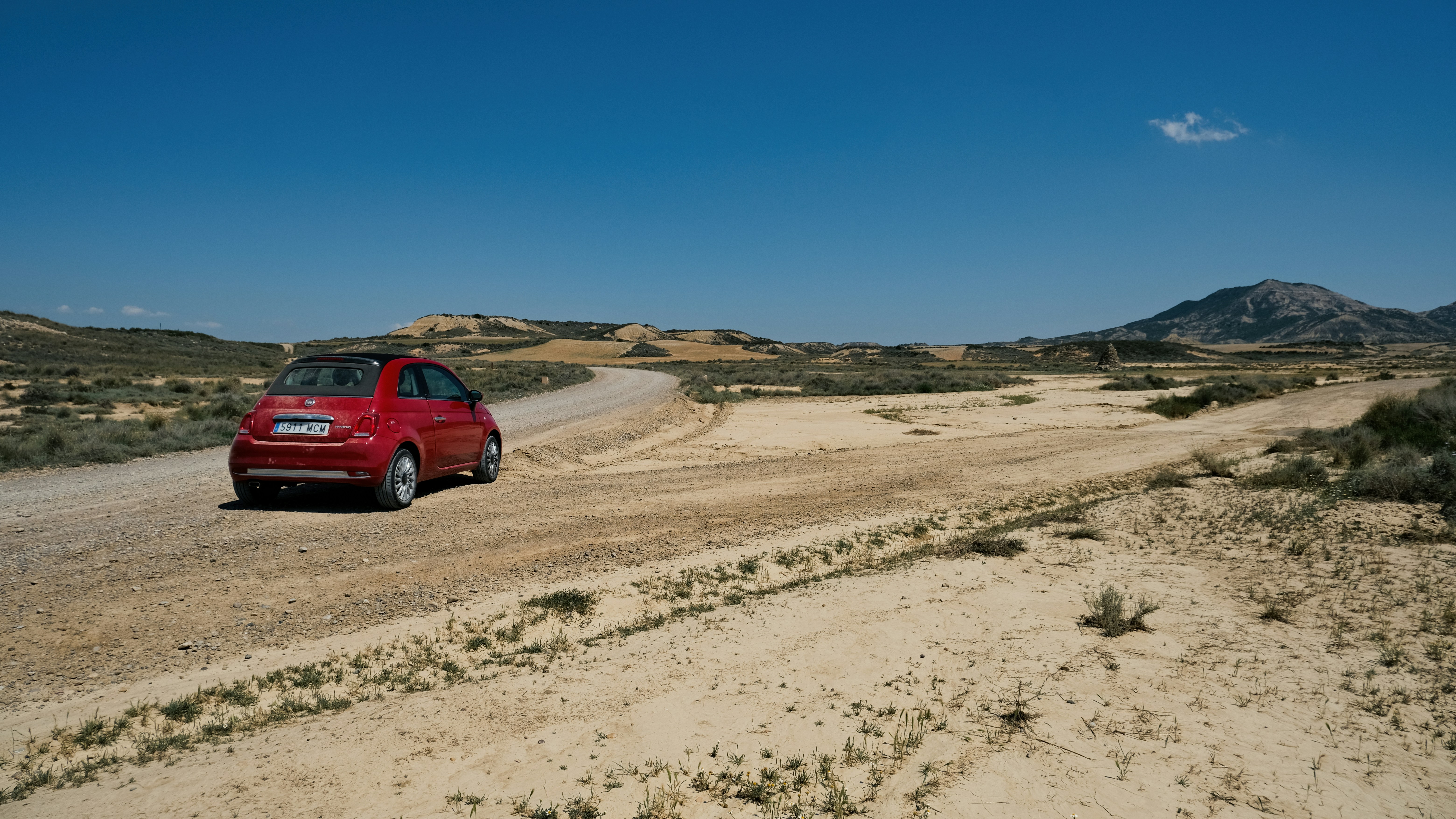 Red car driving on a dirt road in a desert