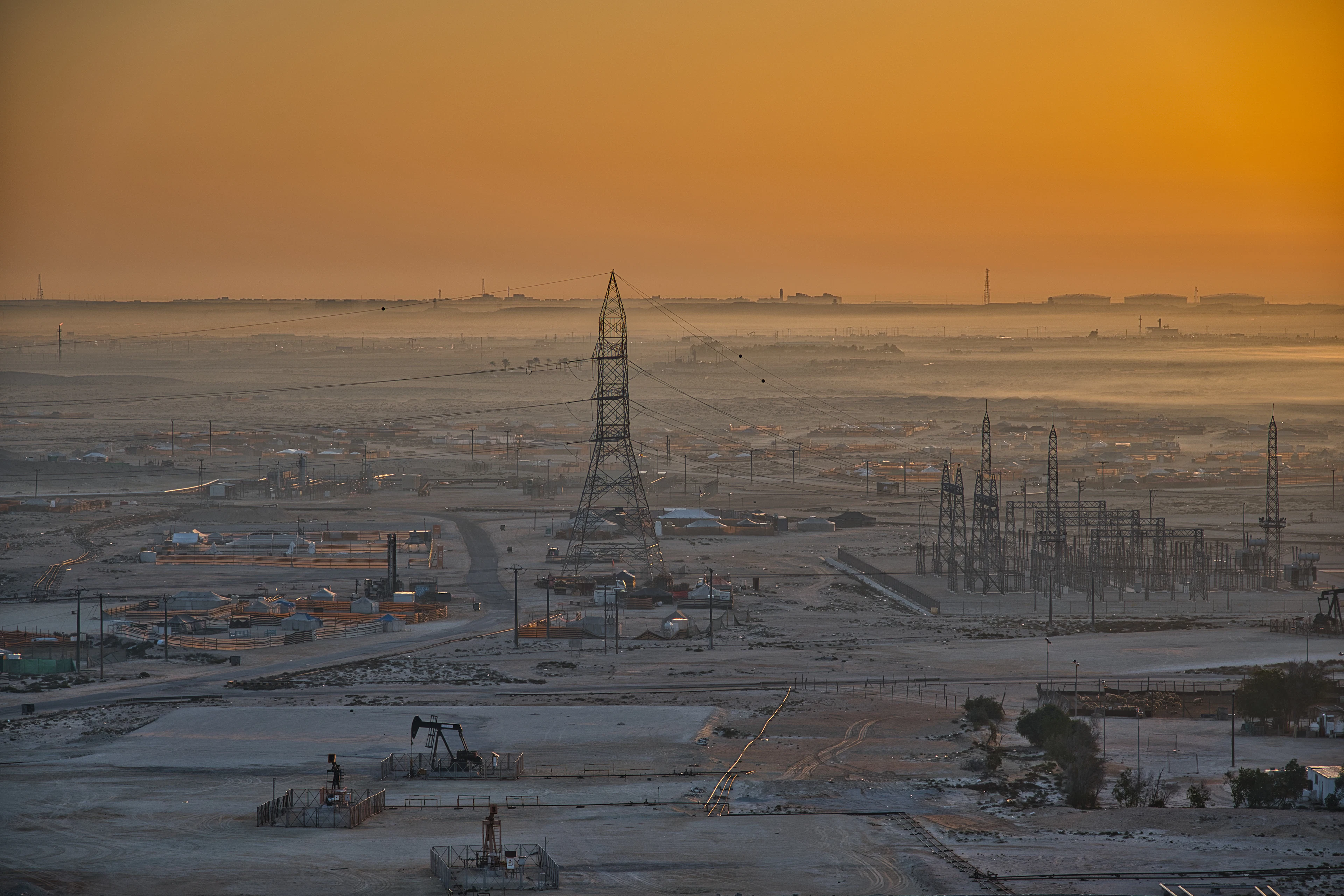 A wide oilfield with pump jacks and power lines under a hazy sunrise