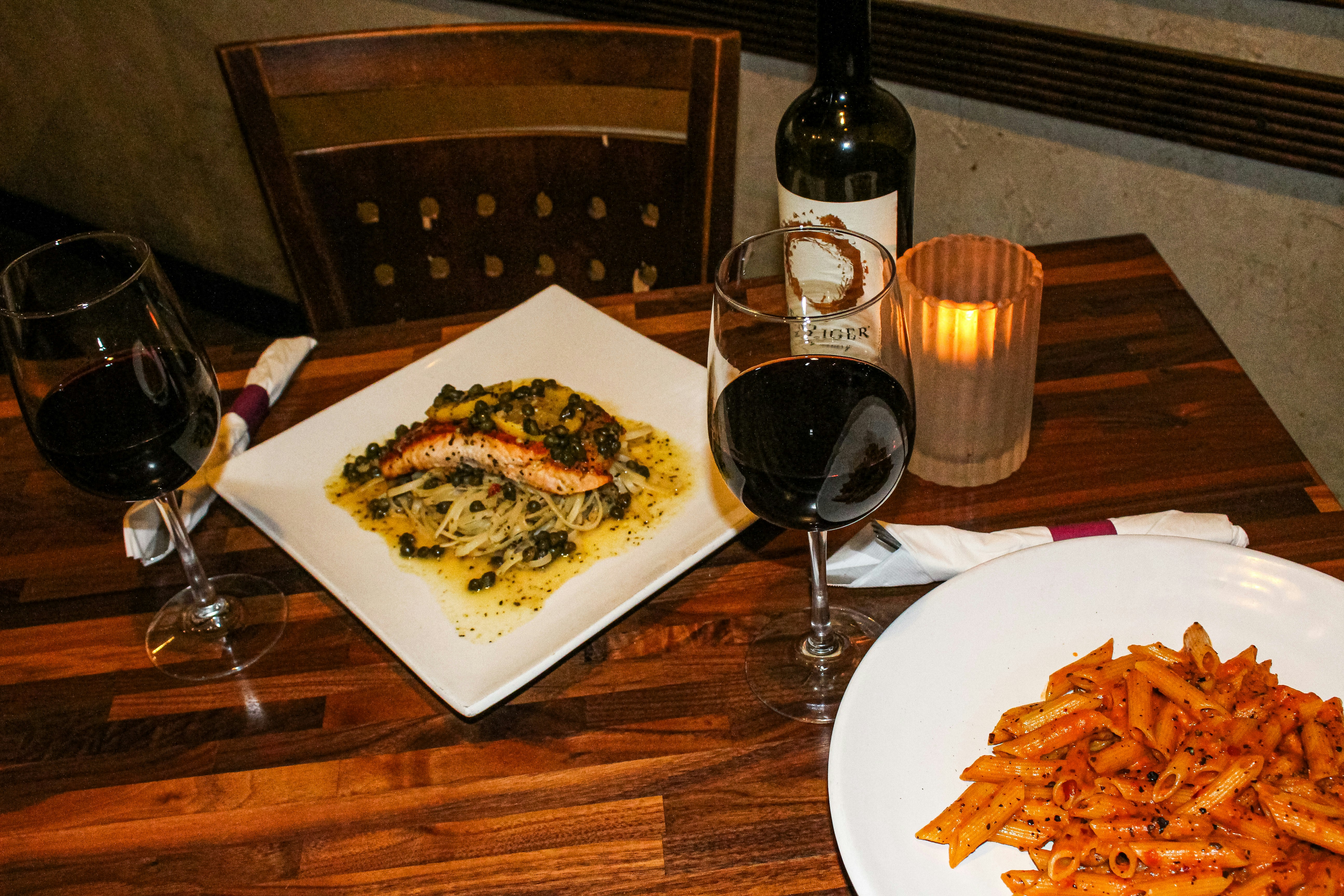 Two glasses of red wine and pasta dishes on table