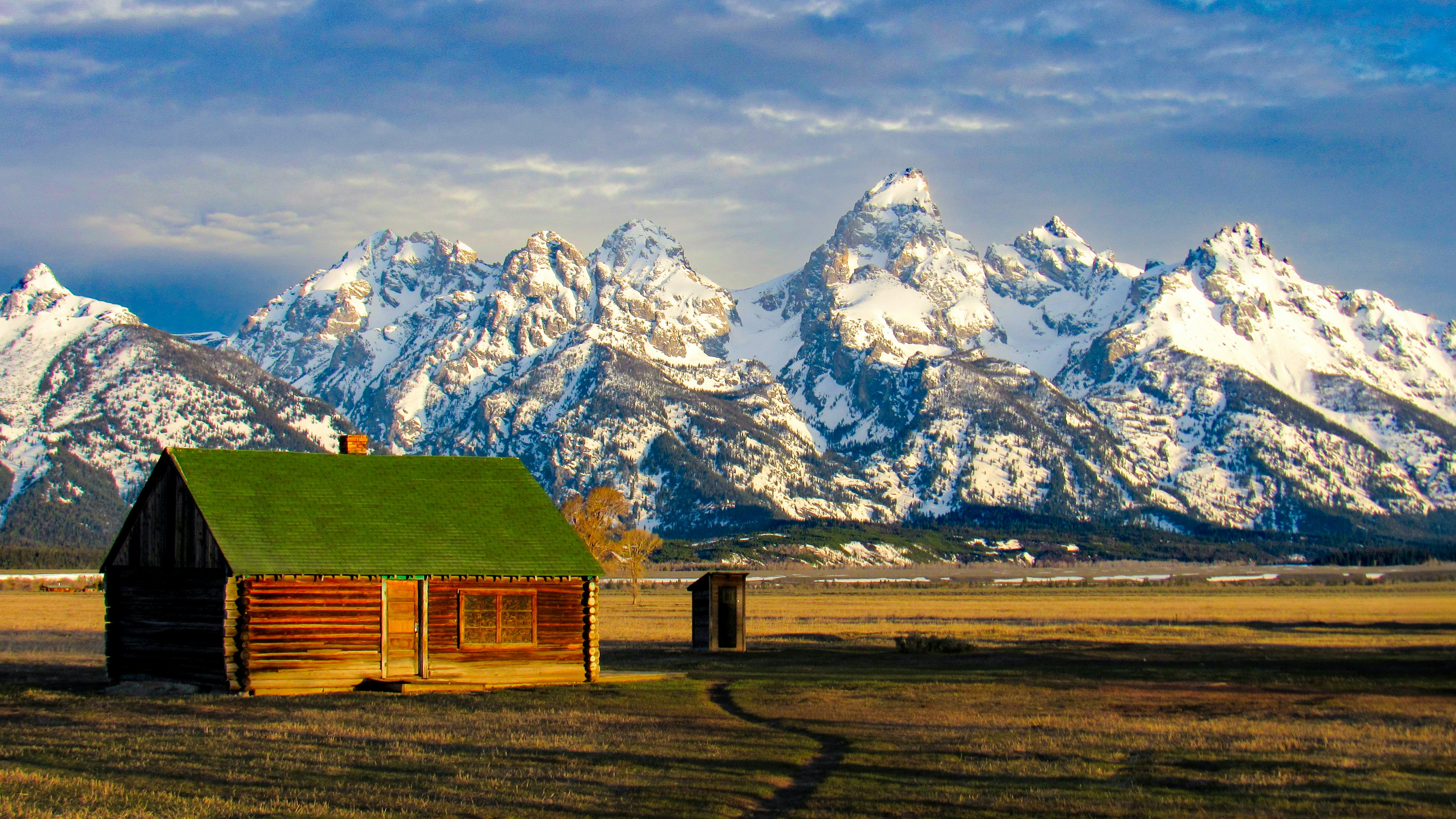 Wooden cabin with green roof near snowy mountains