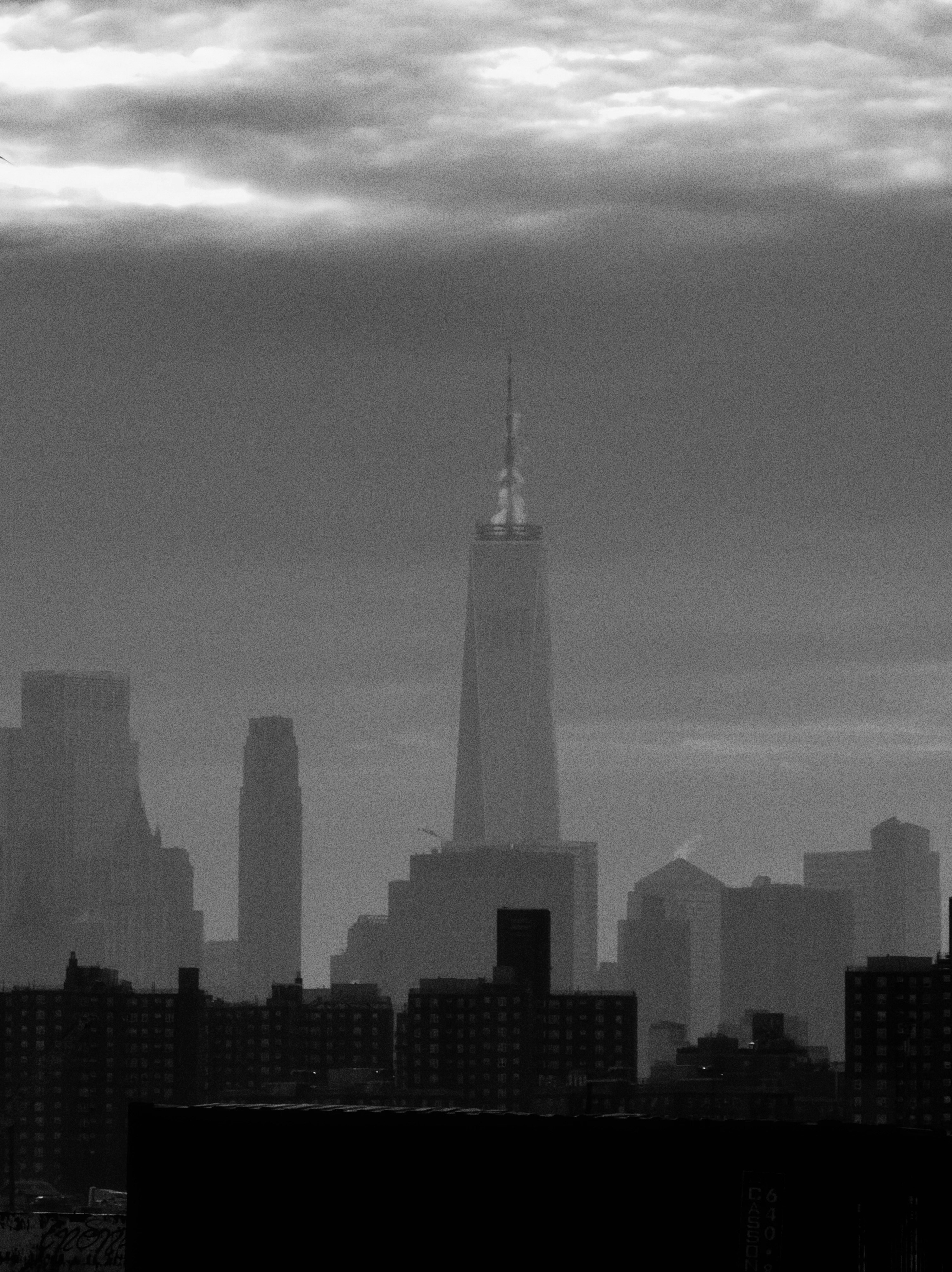 Silhouetted cityscape with a tall skyscraper under cloudy sky
