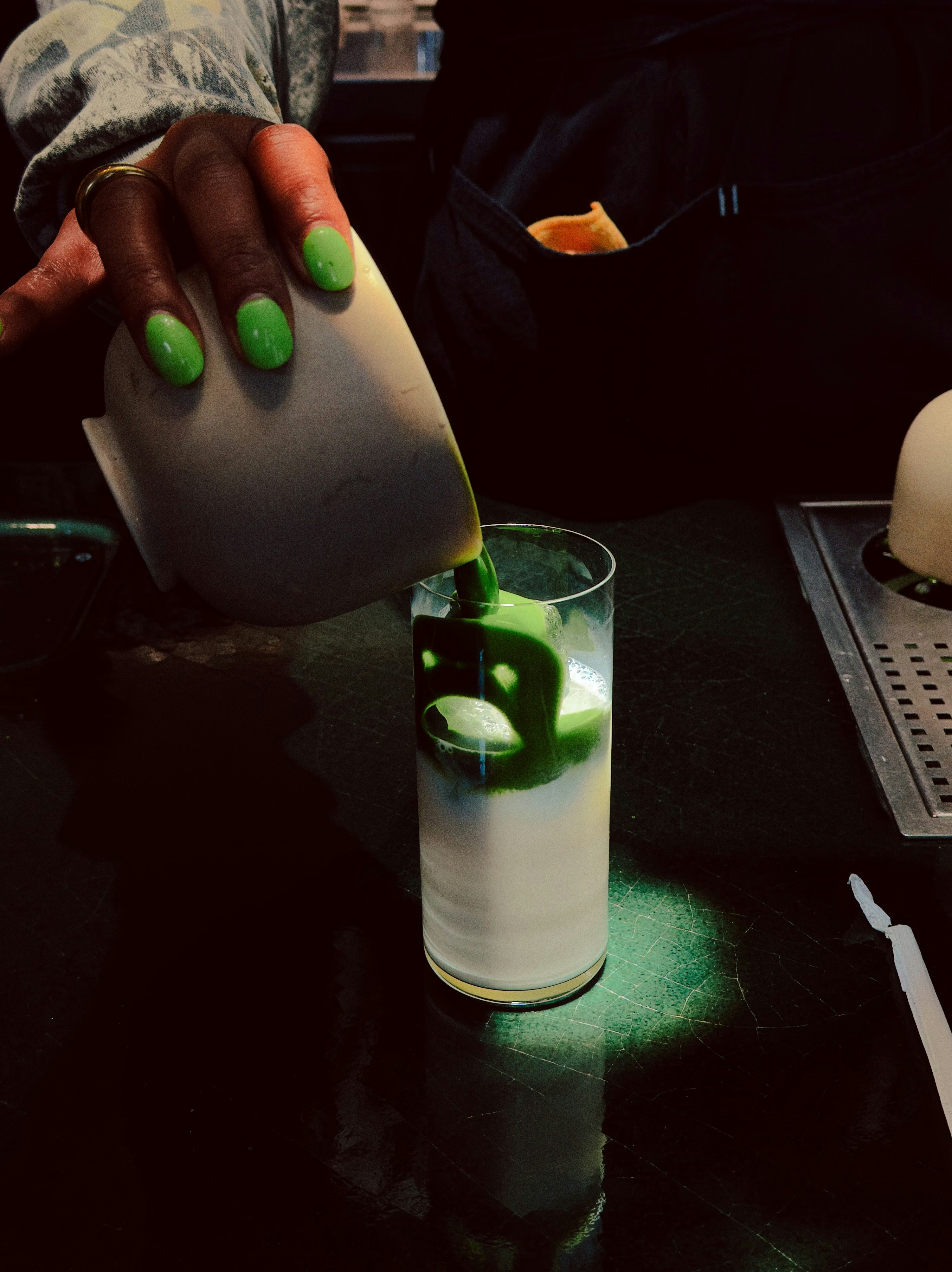 Barista pouring green liquid into a glass of milk.