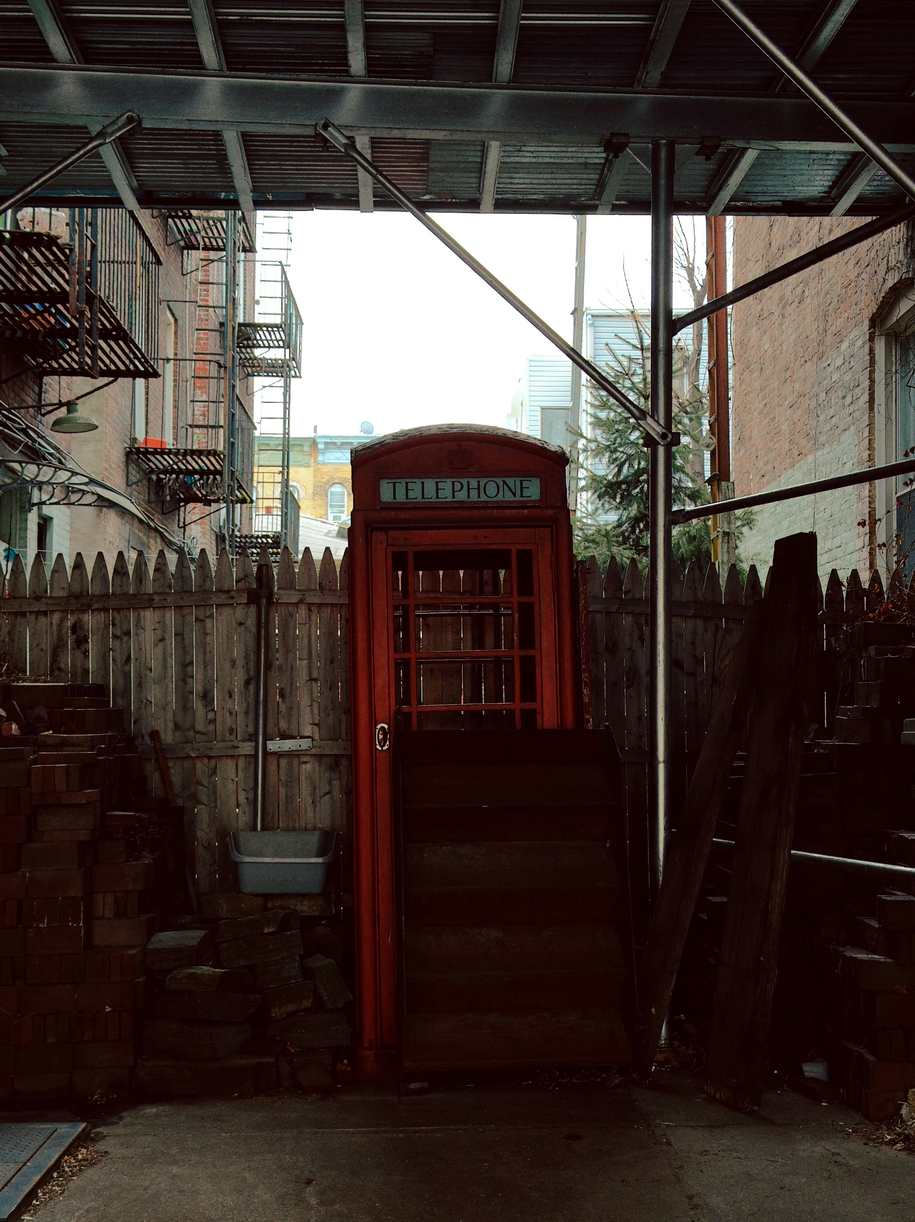Red telephone booth on stairs in urban alley.
