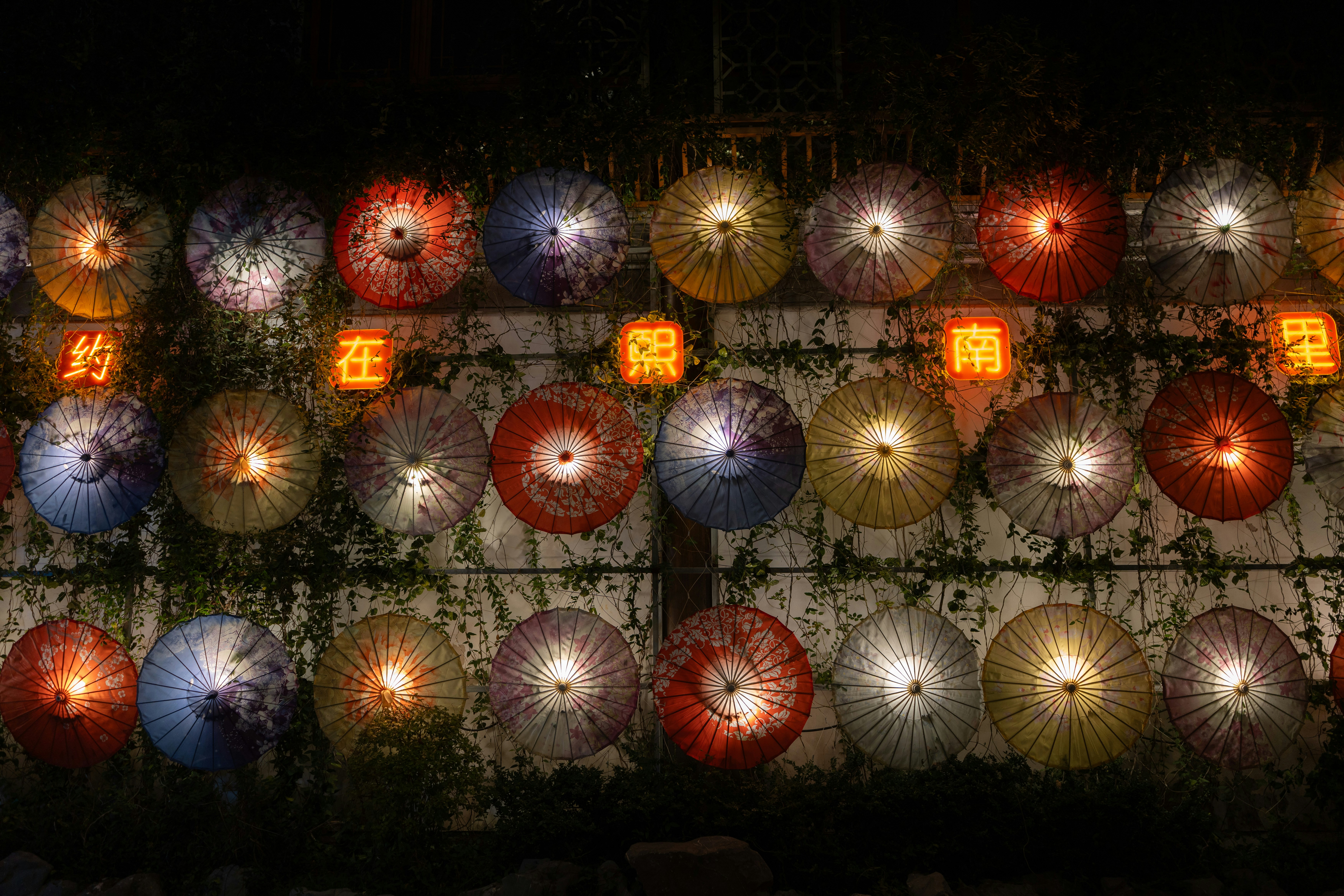 Colorful illuminated umbrellas arranged on a wall at night