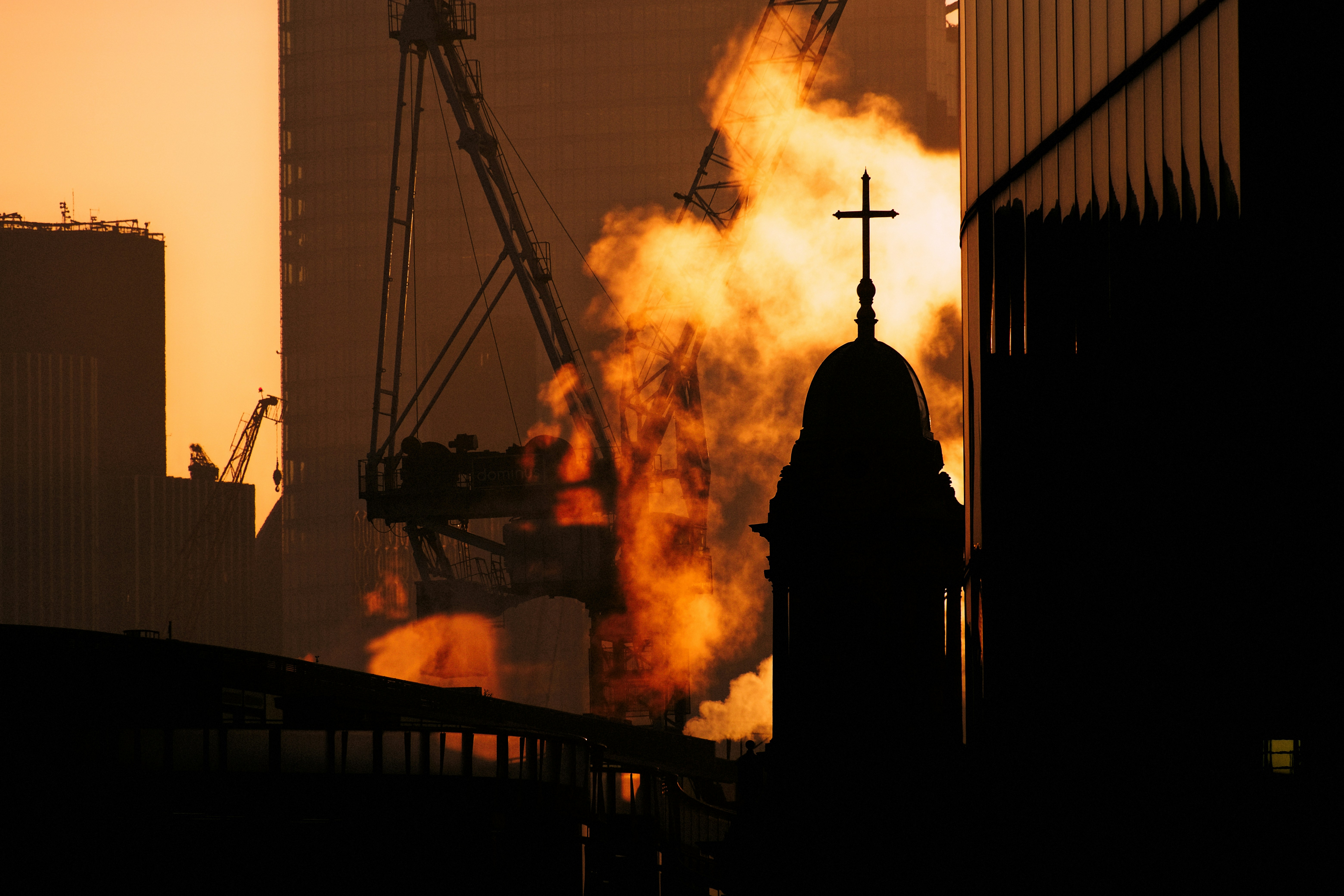 Silhouette eines Kirchturms vor einem feurigen industriellen Hintergrund.
