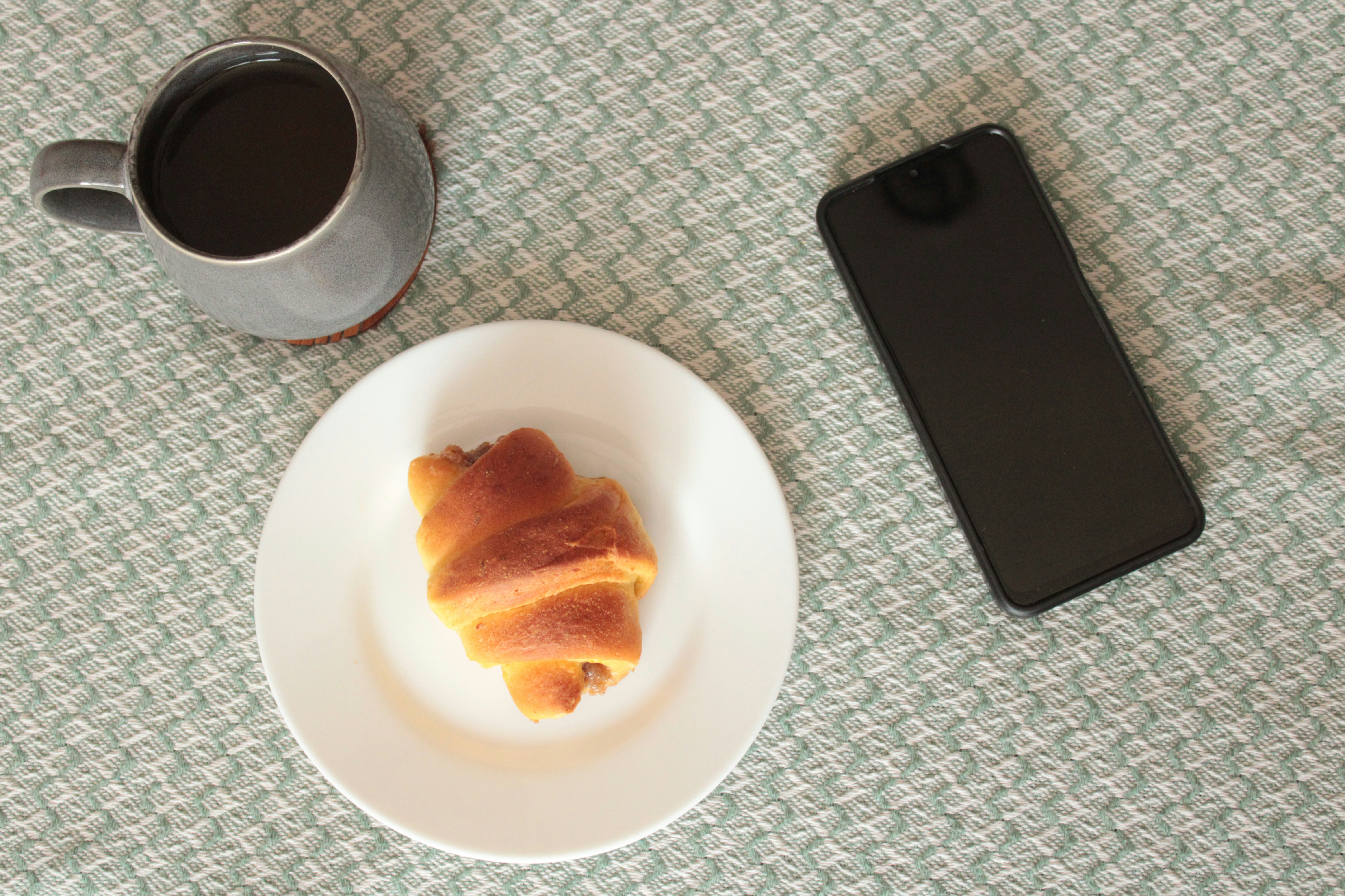 Café e croissant com um smartphone em uma superfície estampada