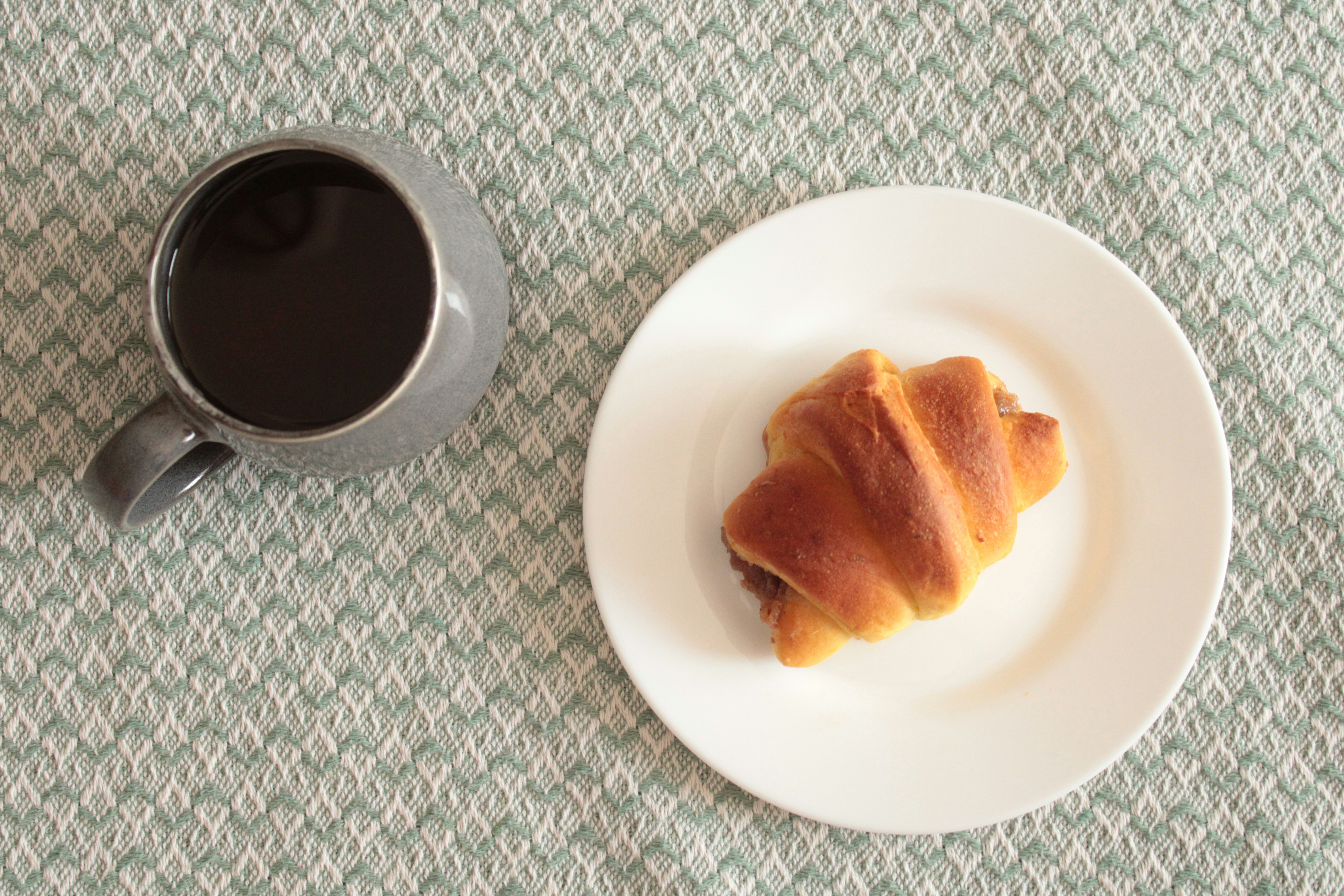 Uma xícara de café e um croissant em um prato.