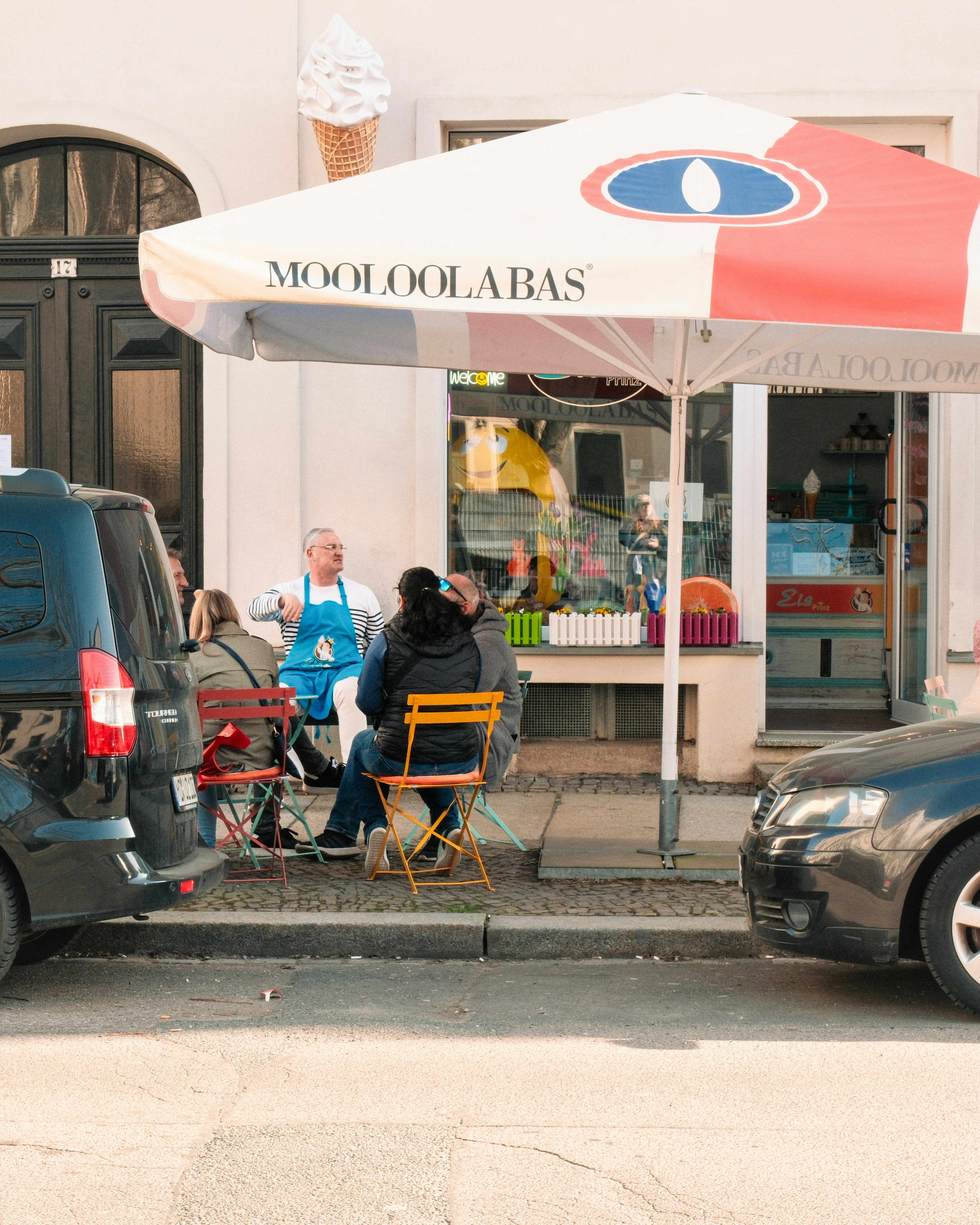 Die Leute sitzen draußen vor einer Eisdiele unter einem Regenschirm.
