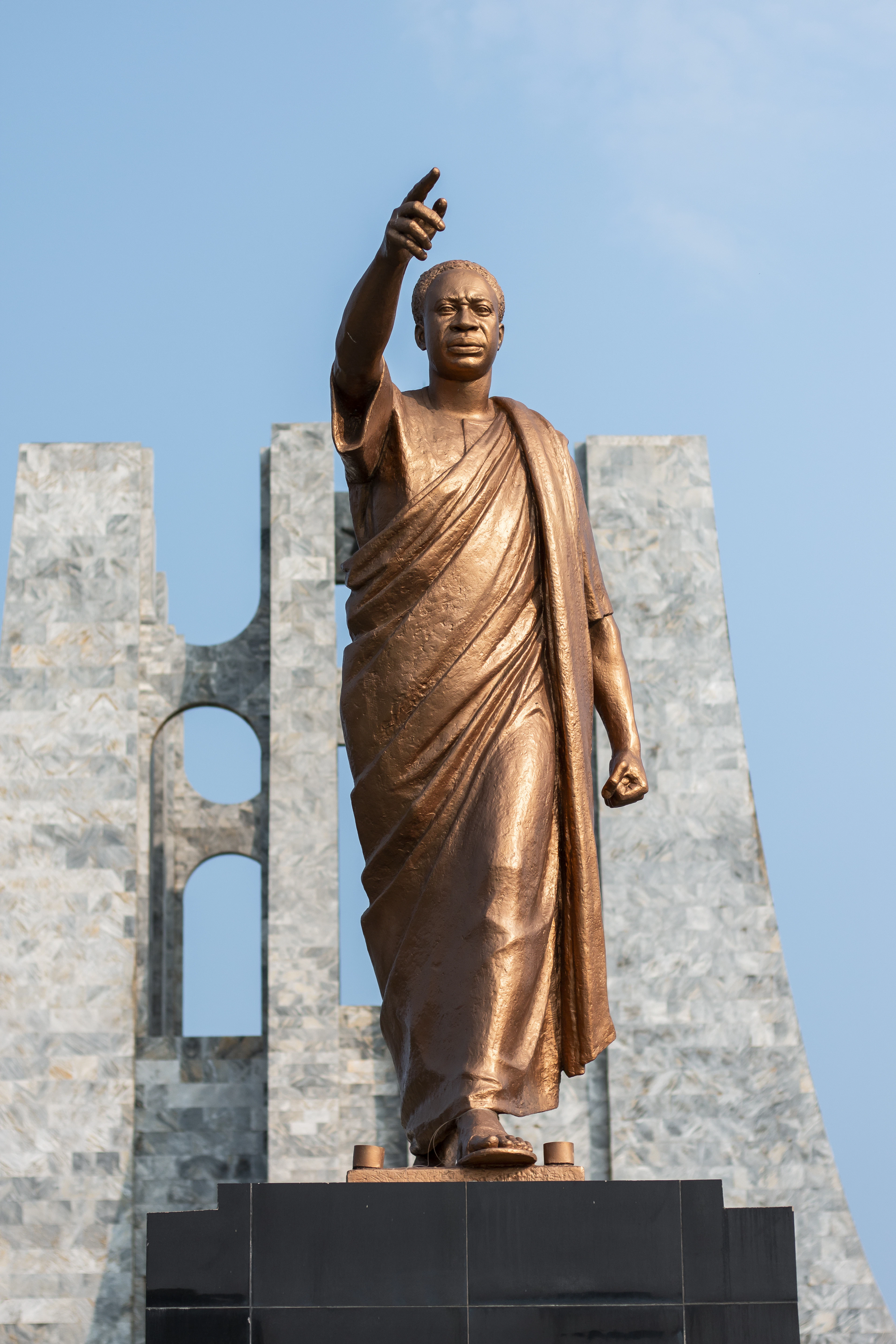 Bronze statue of Kwame Nkrumah with arm raised, backed by the white stone arches of his Accra memorial park.