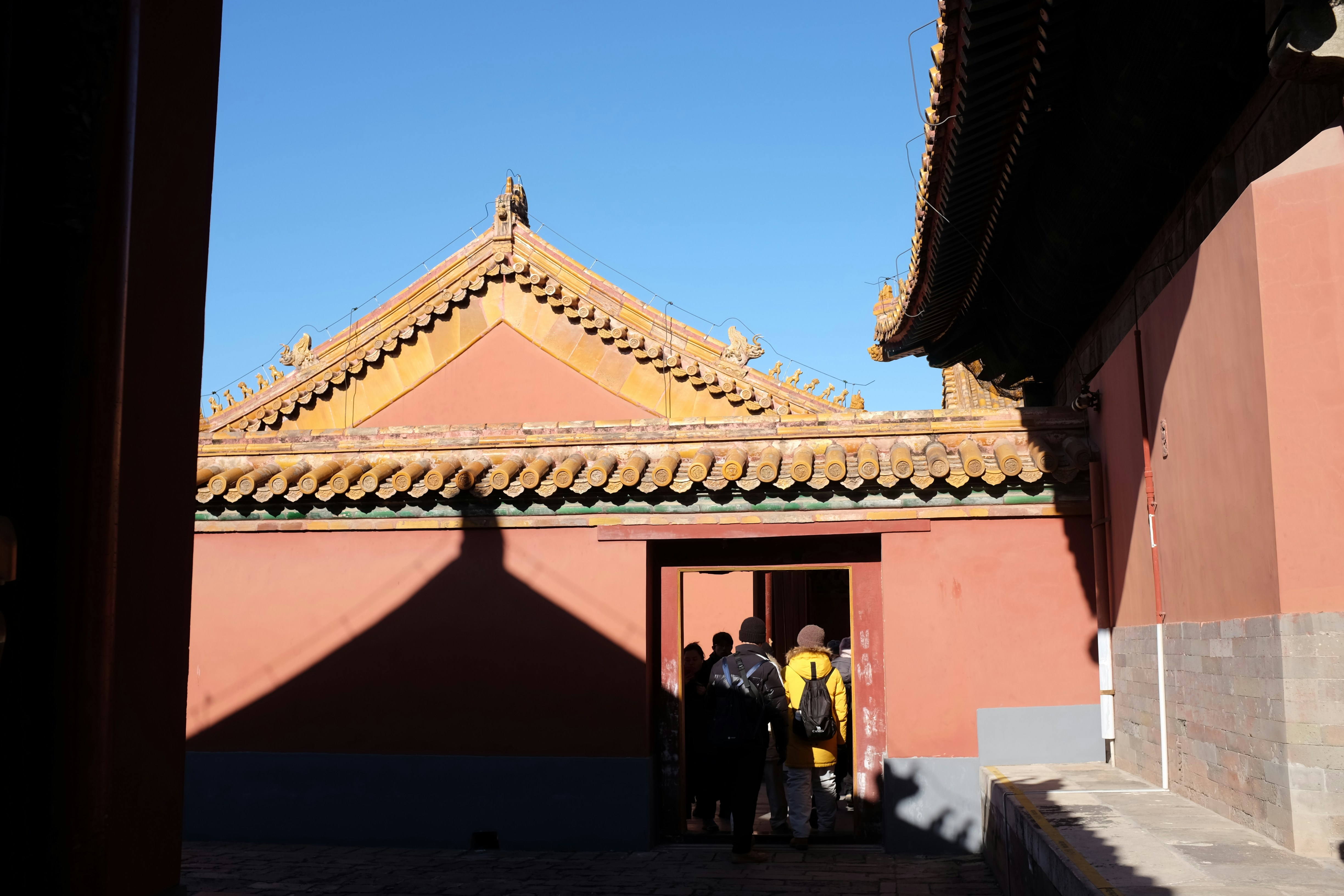 Pessoas entrando em um prédio tradicional vermelho com telhado de telhas amarelas.