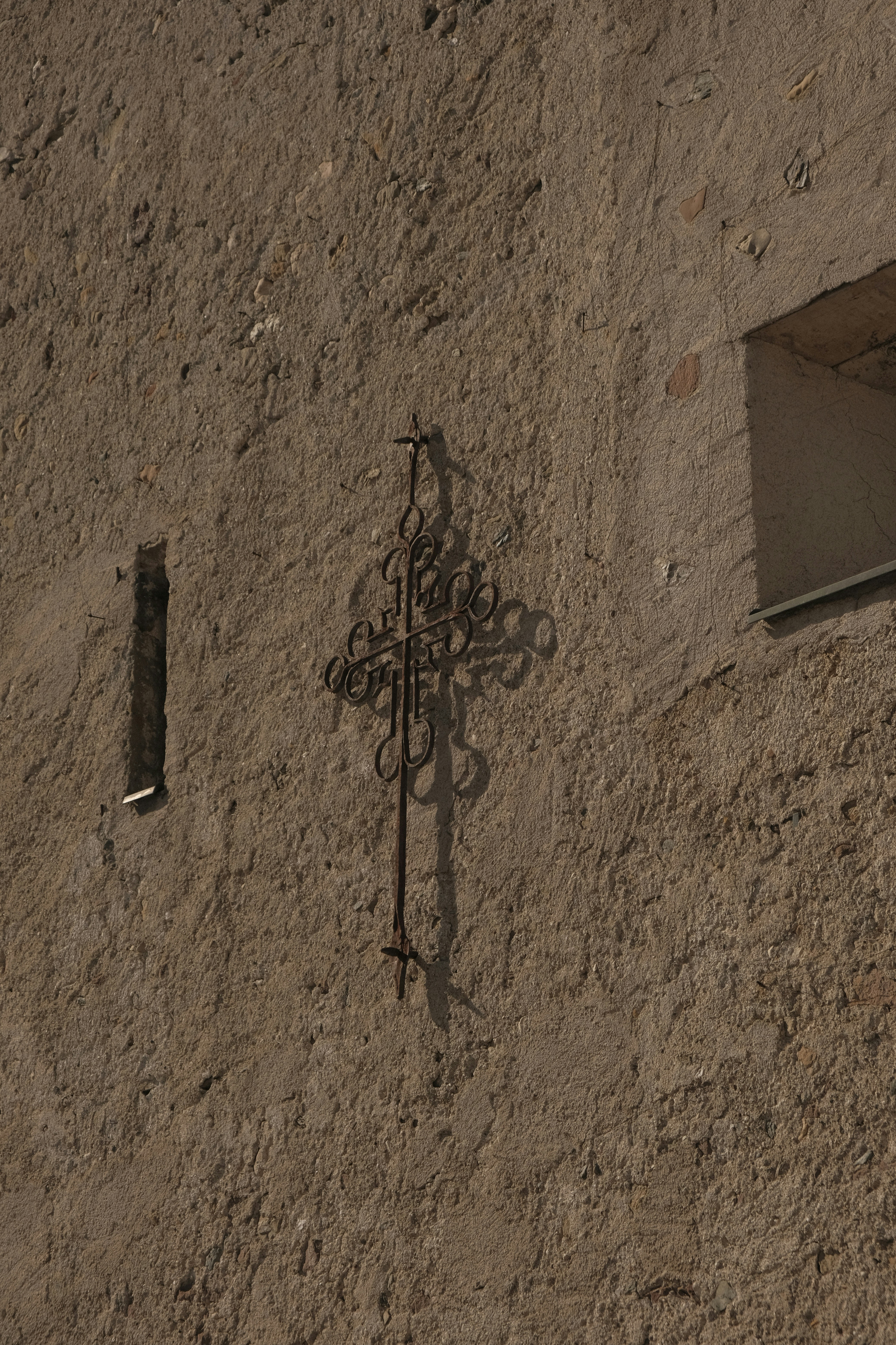 Ornate metal cross affixed to a textured stone wall.