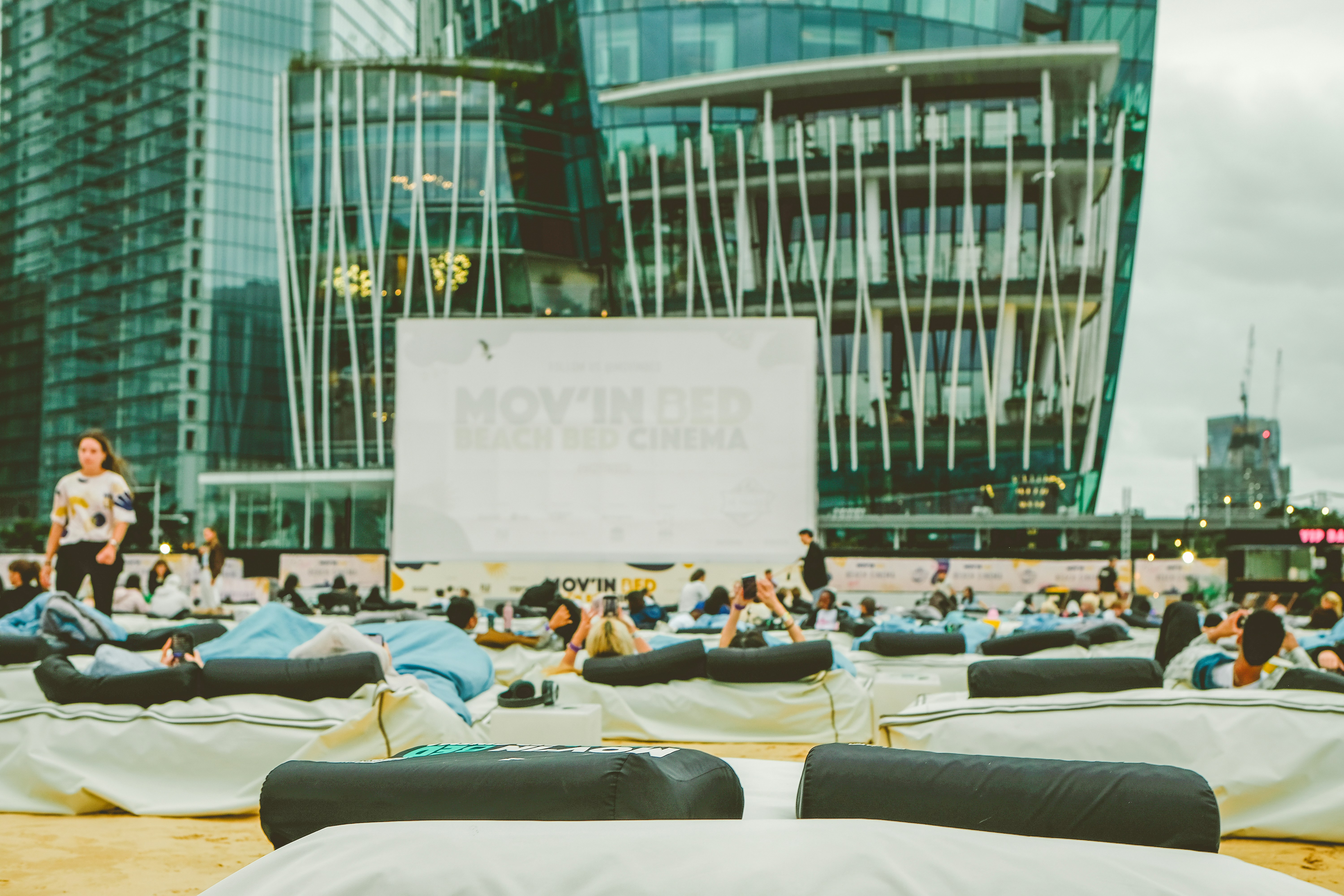 Pessoas relaxando em almofadas durante uma exibição de filme ao ar livre.