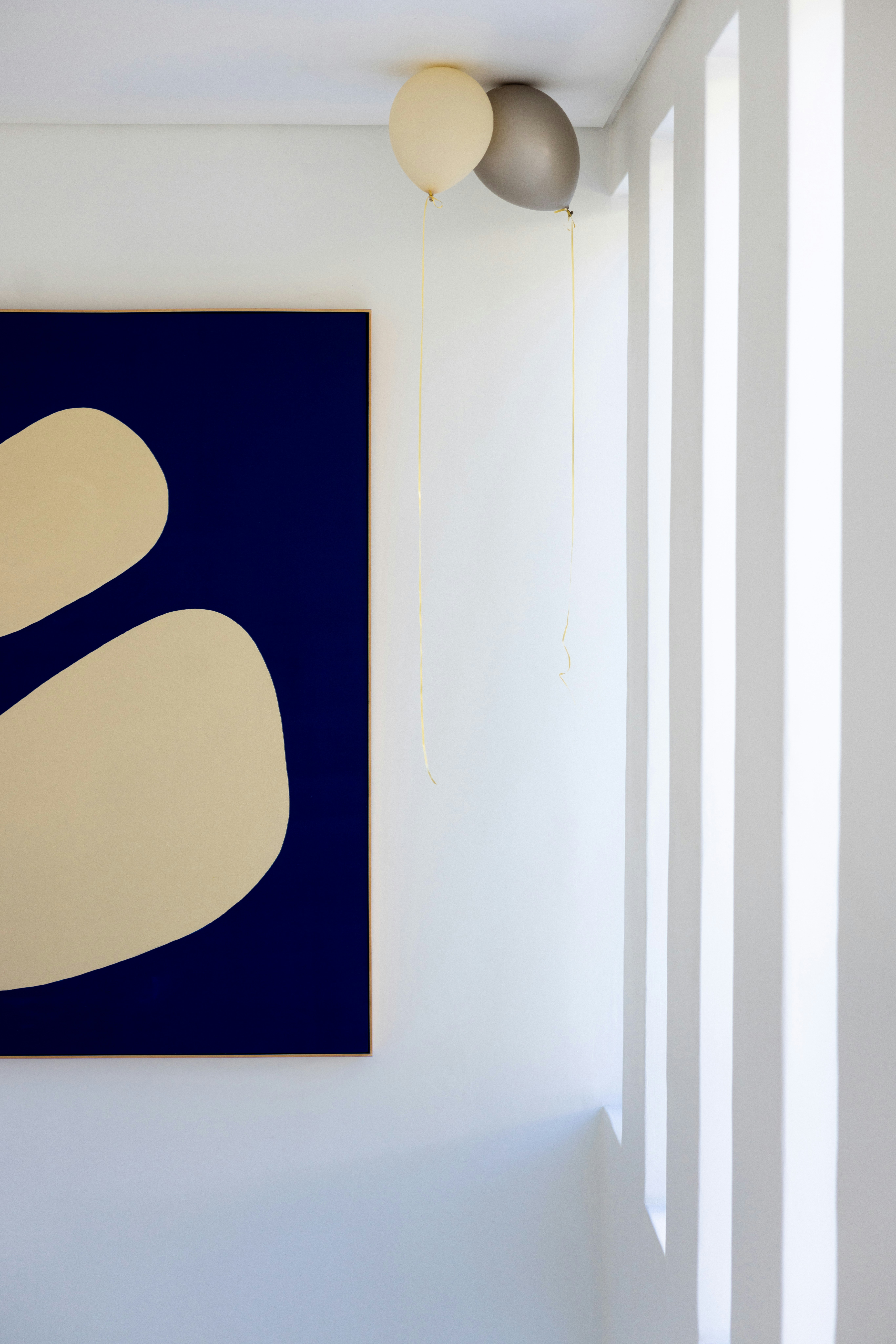 Two balloons float near abstract art on wall.