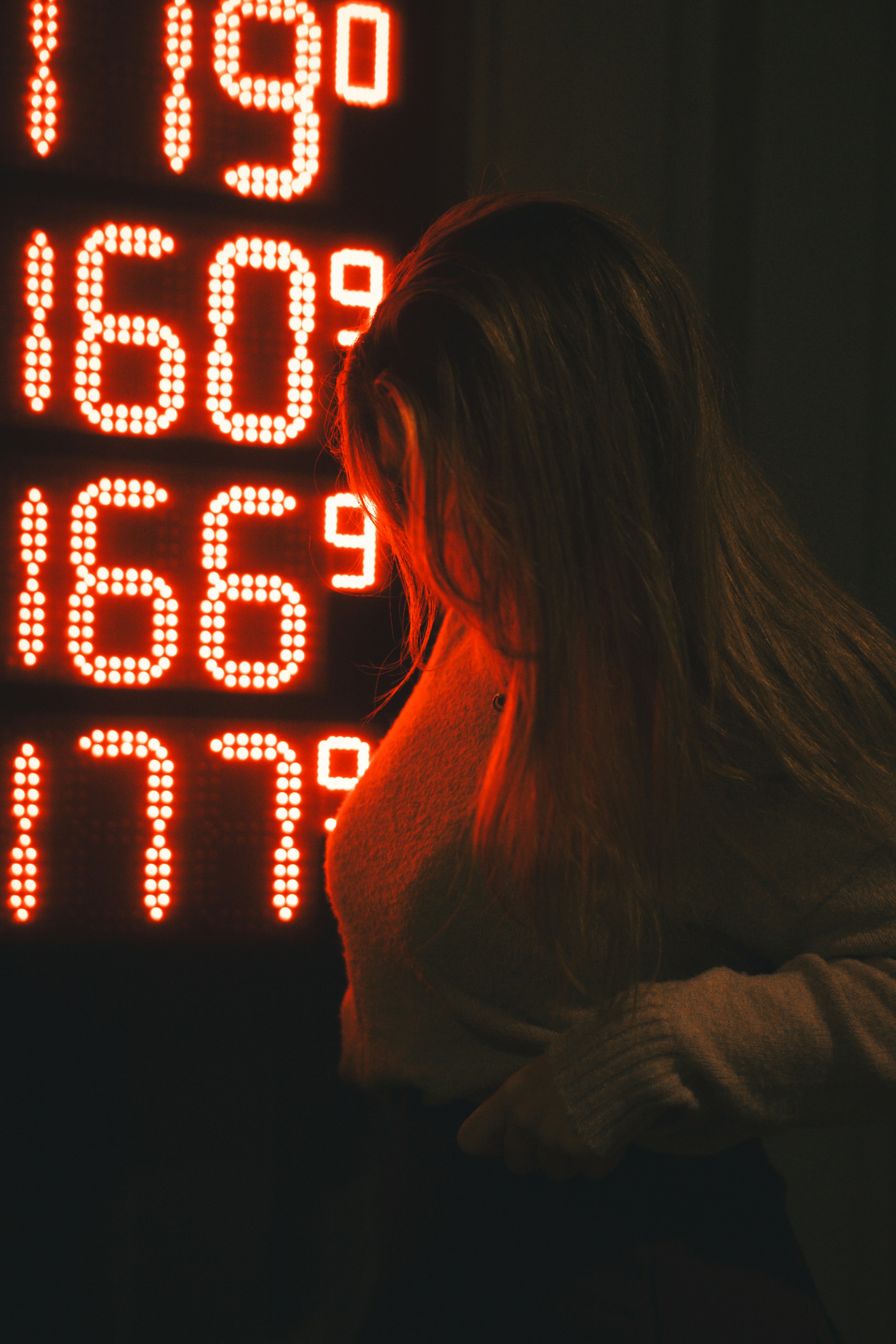 Woman looks at glowing red gas price numbers