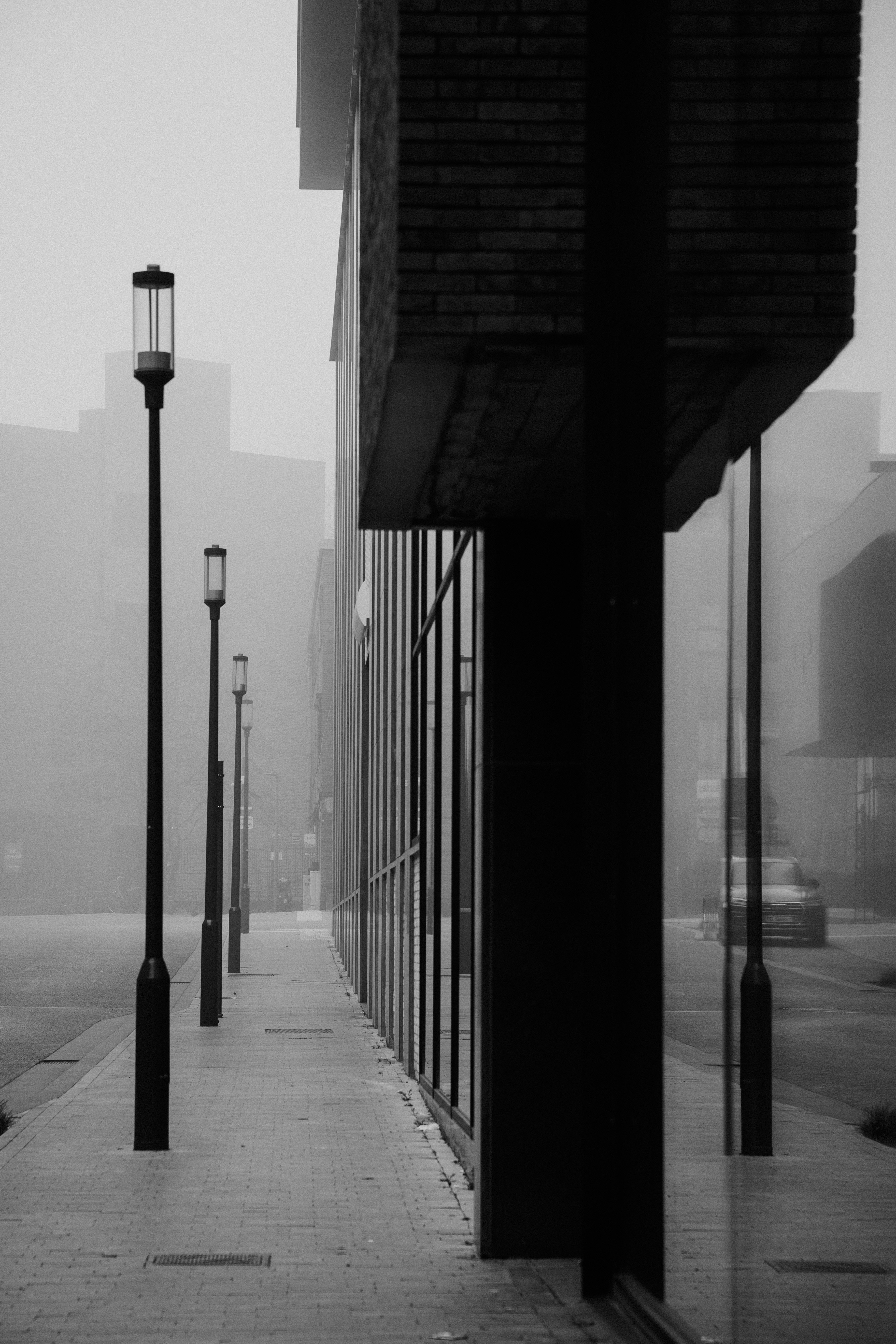 街灯が霧のかかる歩道に並び、現代的な建物の隣に並んでいます。