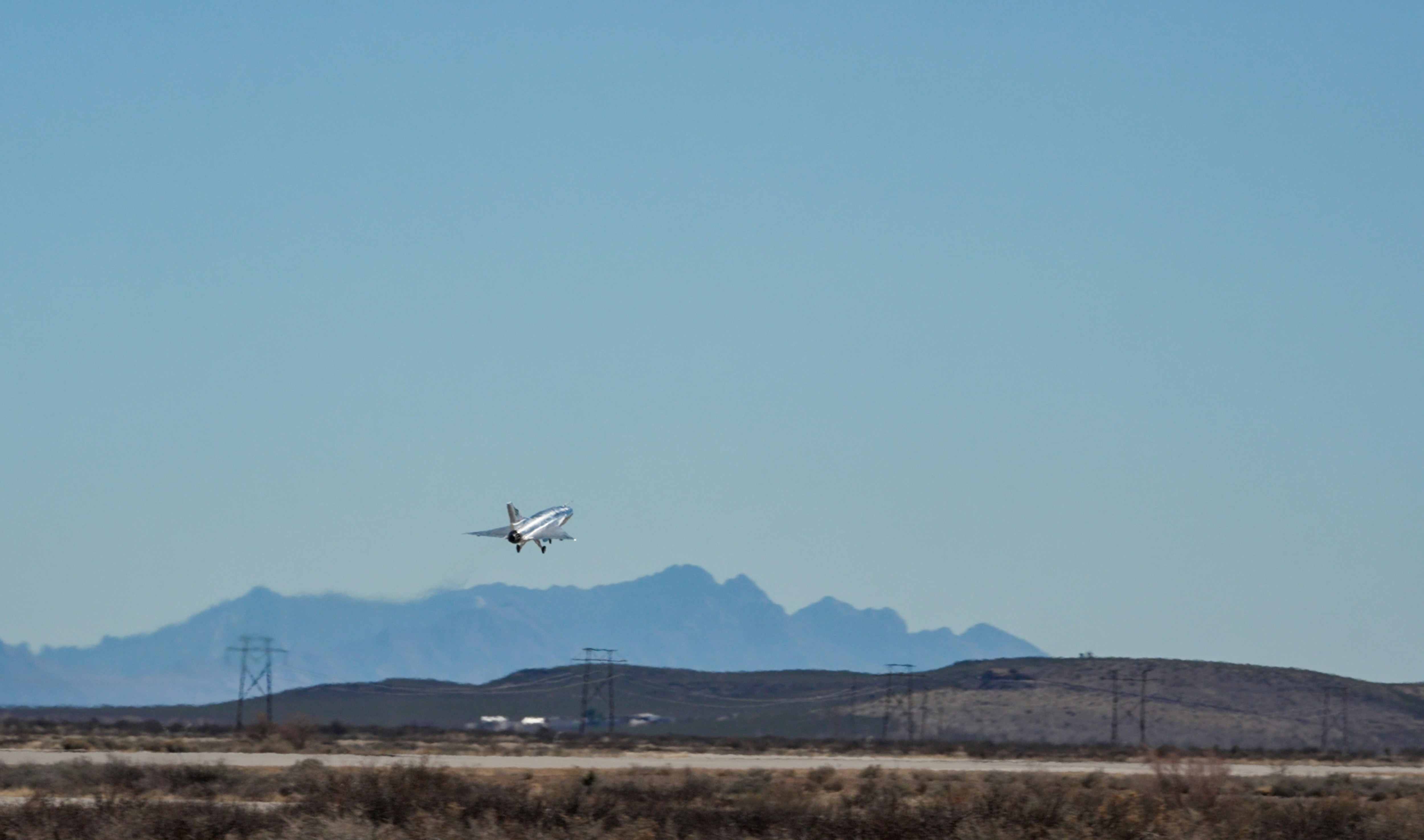 Ein weißes Flugzeug fliegt über eine Wüstenlandschaft.