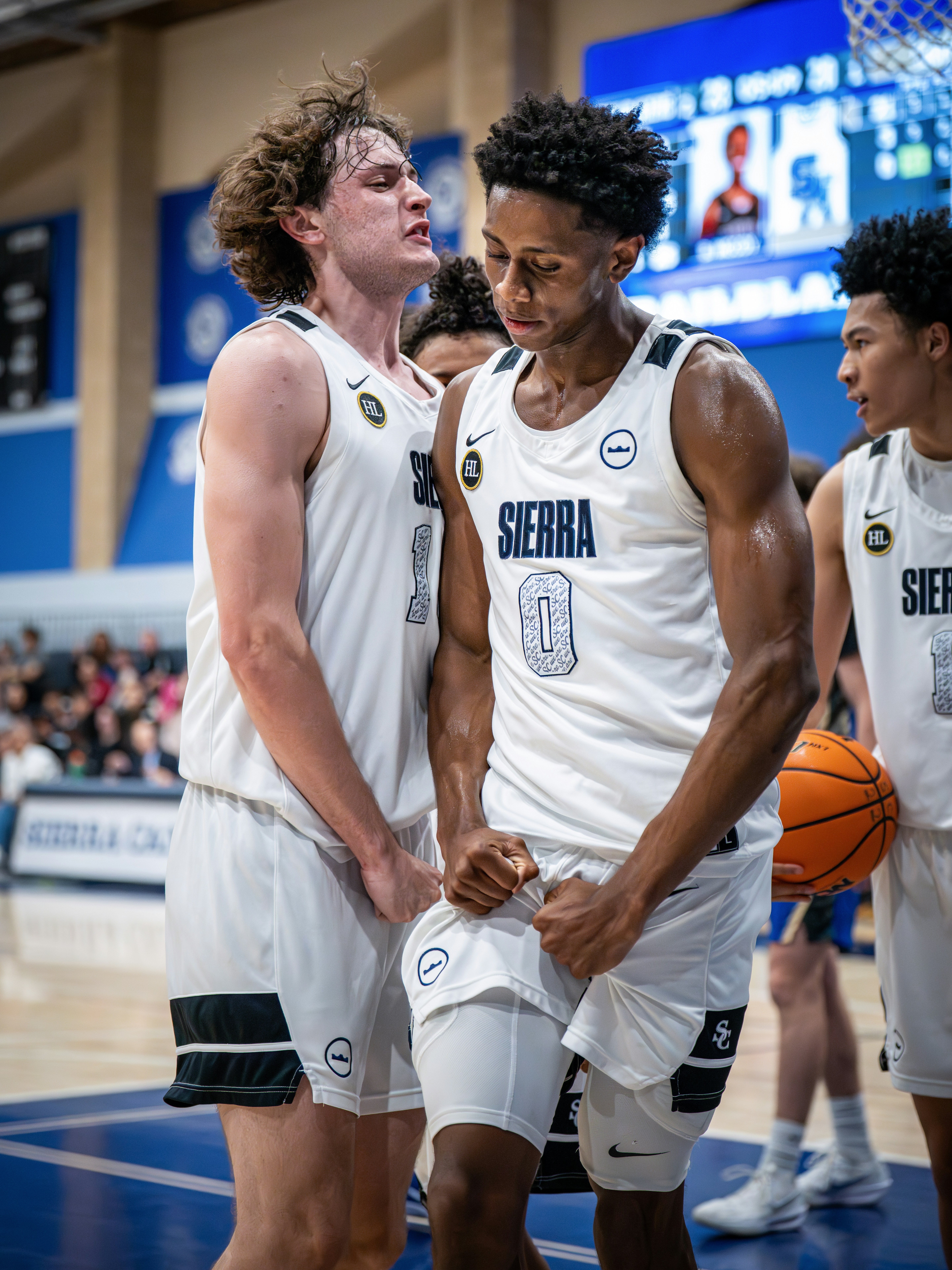Two young basketball players in white uniforms on court.