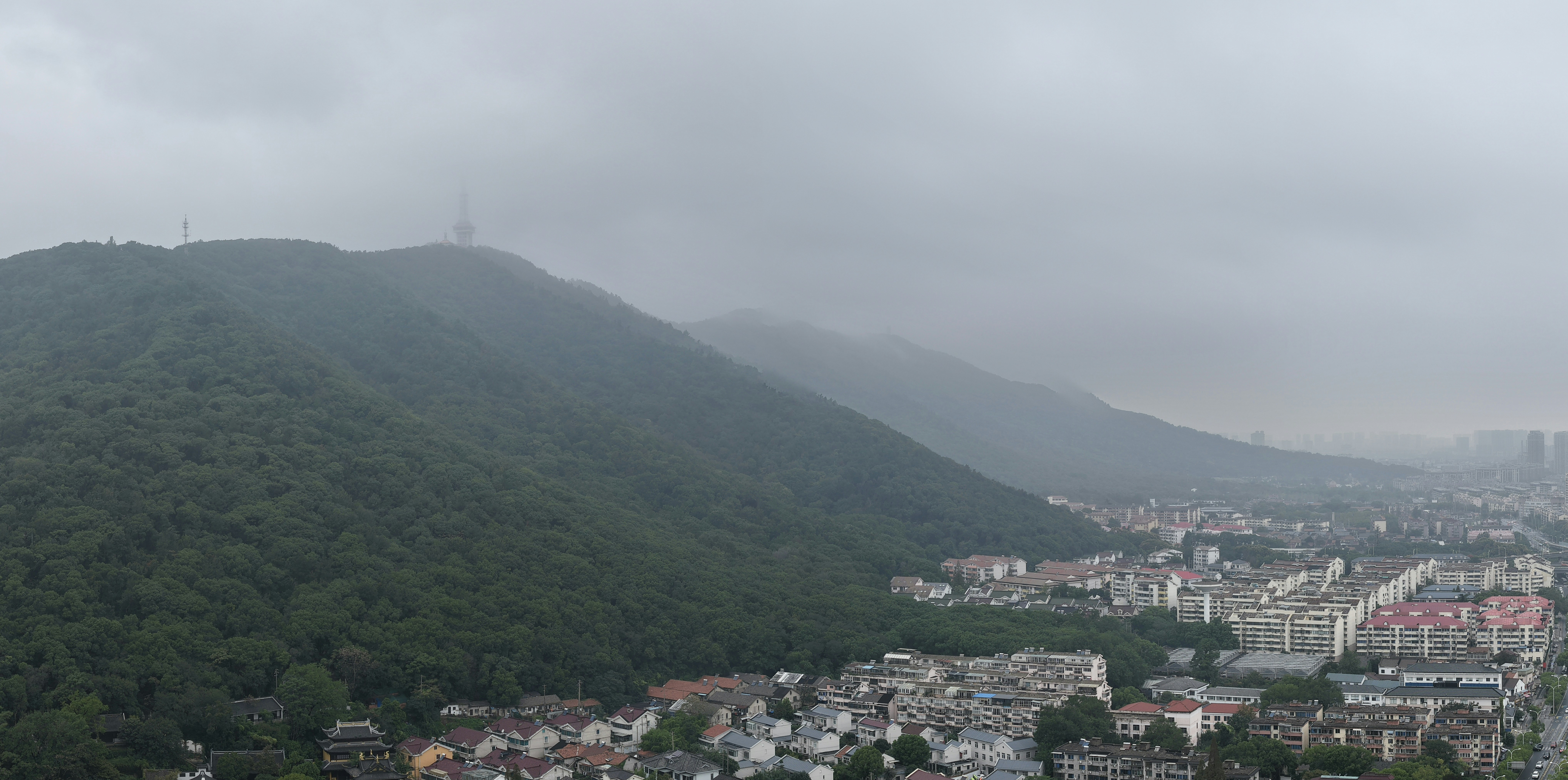 Misty mountains overlook a sprawling city under a cloudy sky.