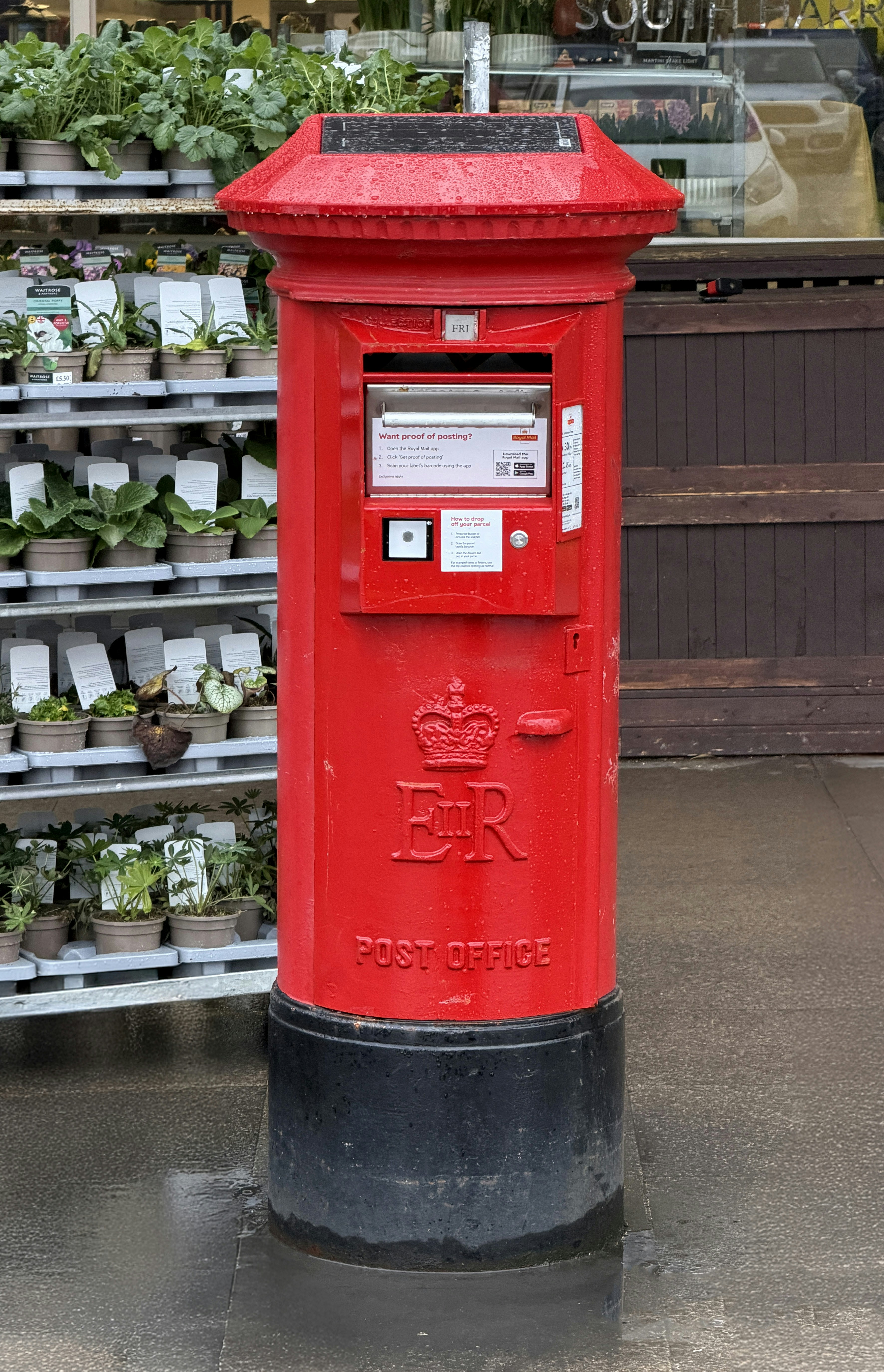 A red british post box with a black base.