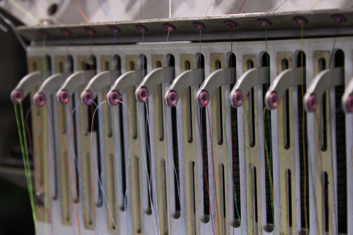 Close-up of an industrial embroidery machine's thread guides — precision stitching in progress