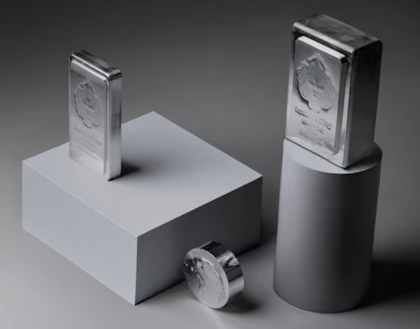 Two silver bars and a coin on pedestals