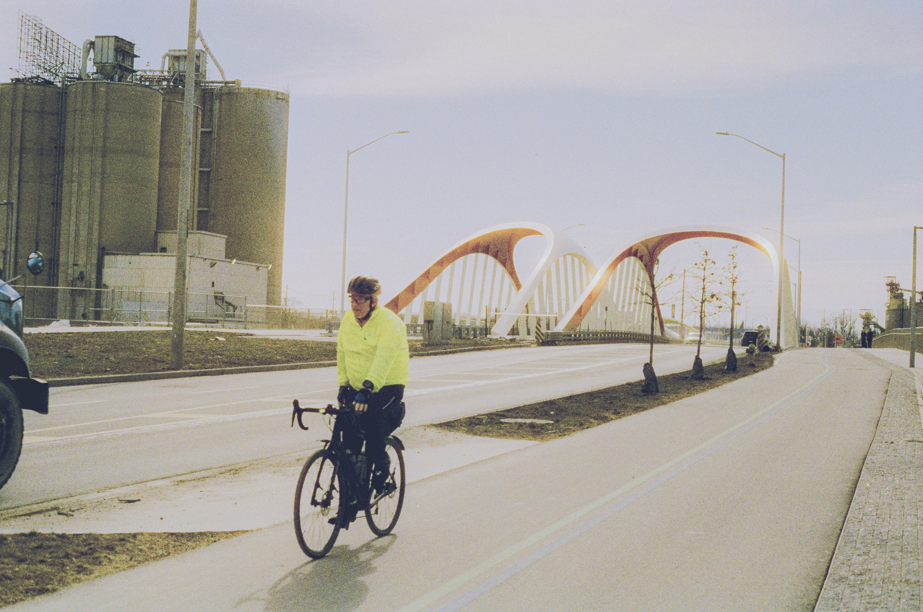 Man in yellow jacket cycles across bridge with silos