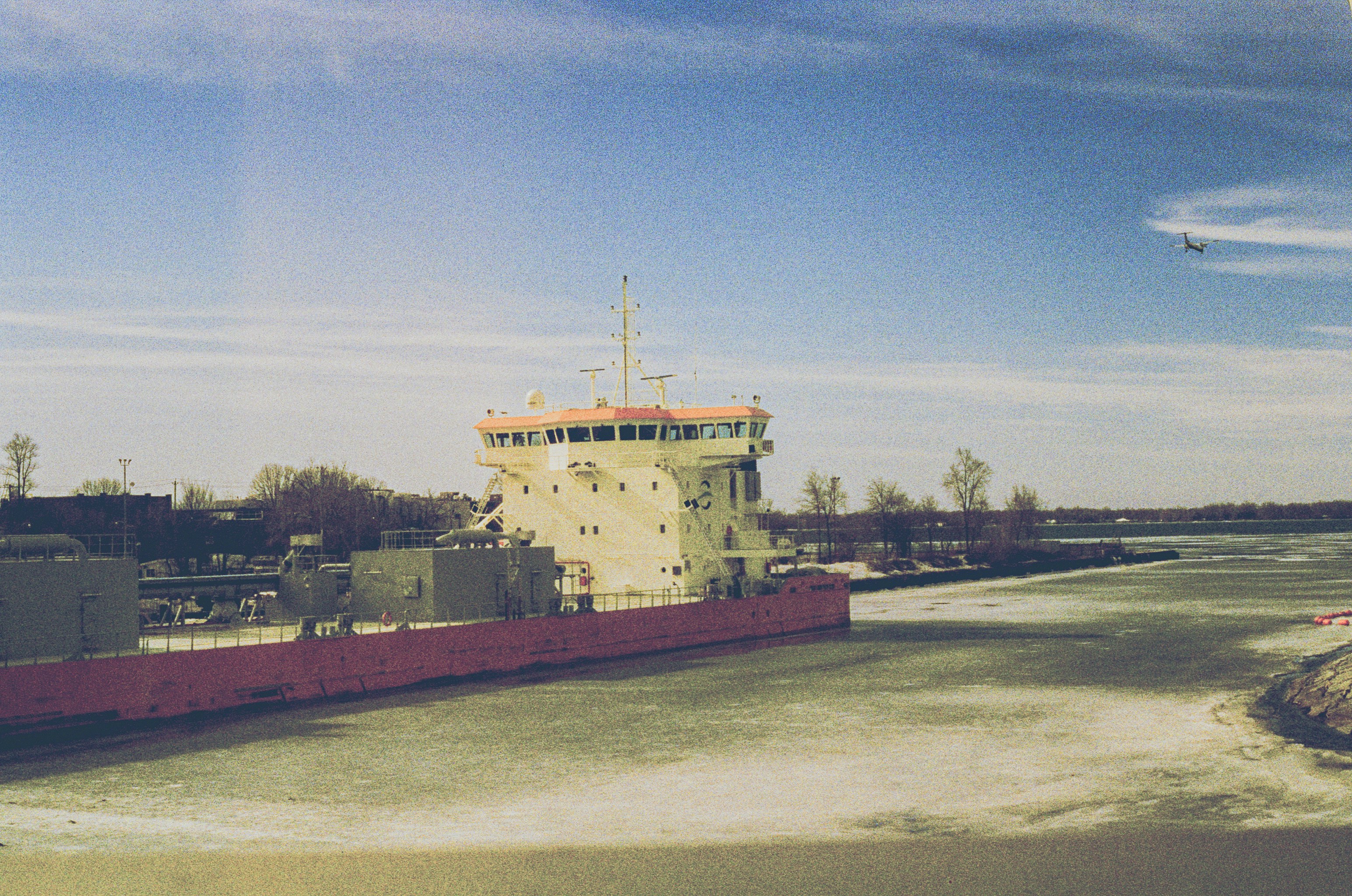 A large cargo ship sails on a partially frozen canal.