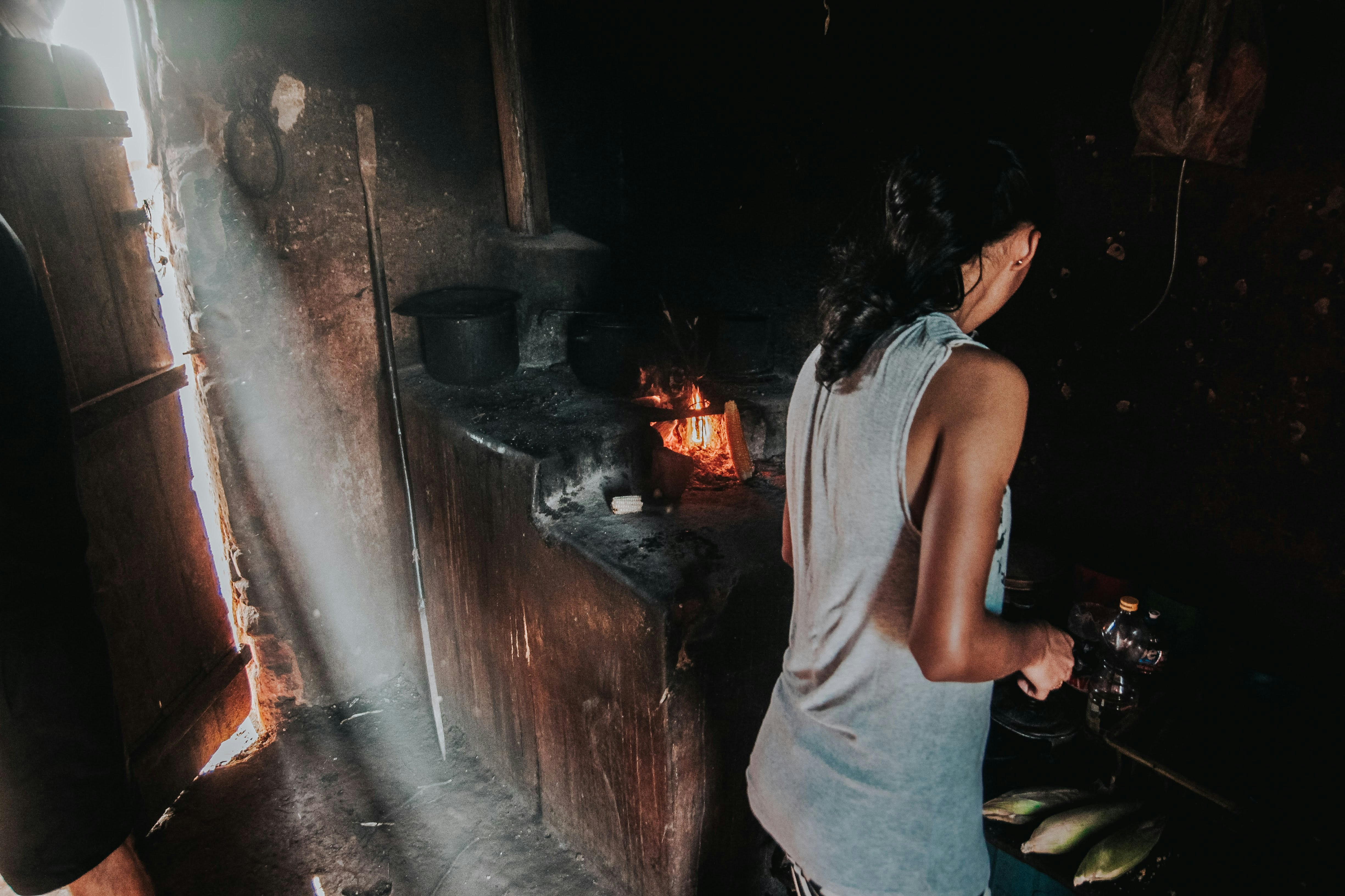 Woman cooking in a rustic, dimly lit kitchen.