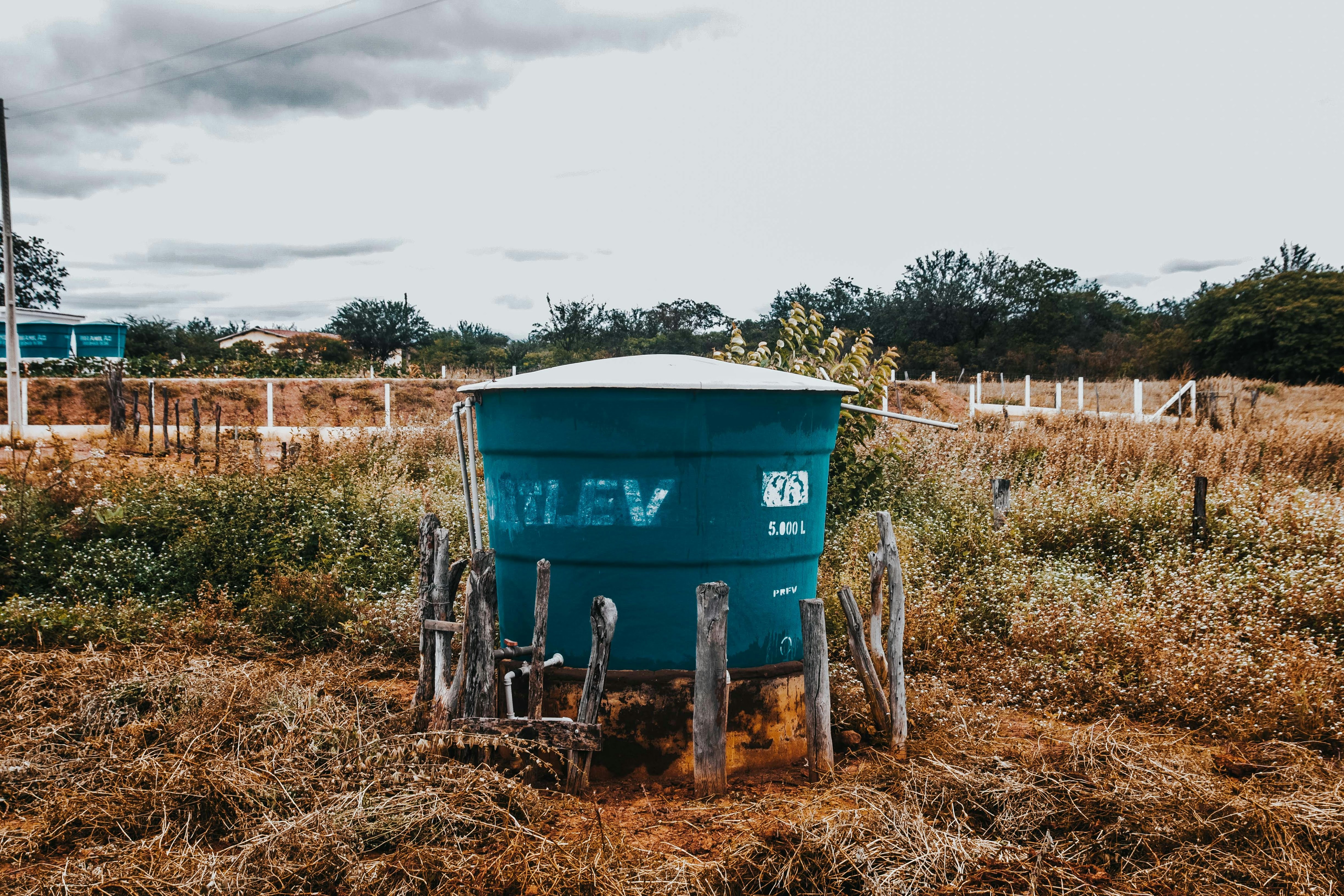 A teal water tank sits in a dry, grassy field.