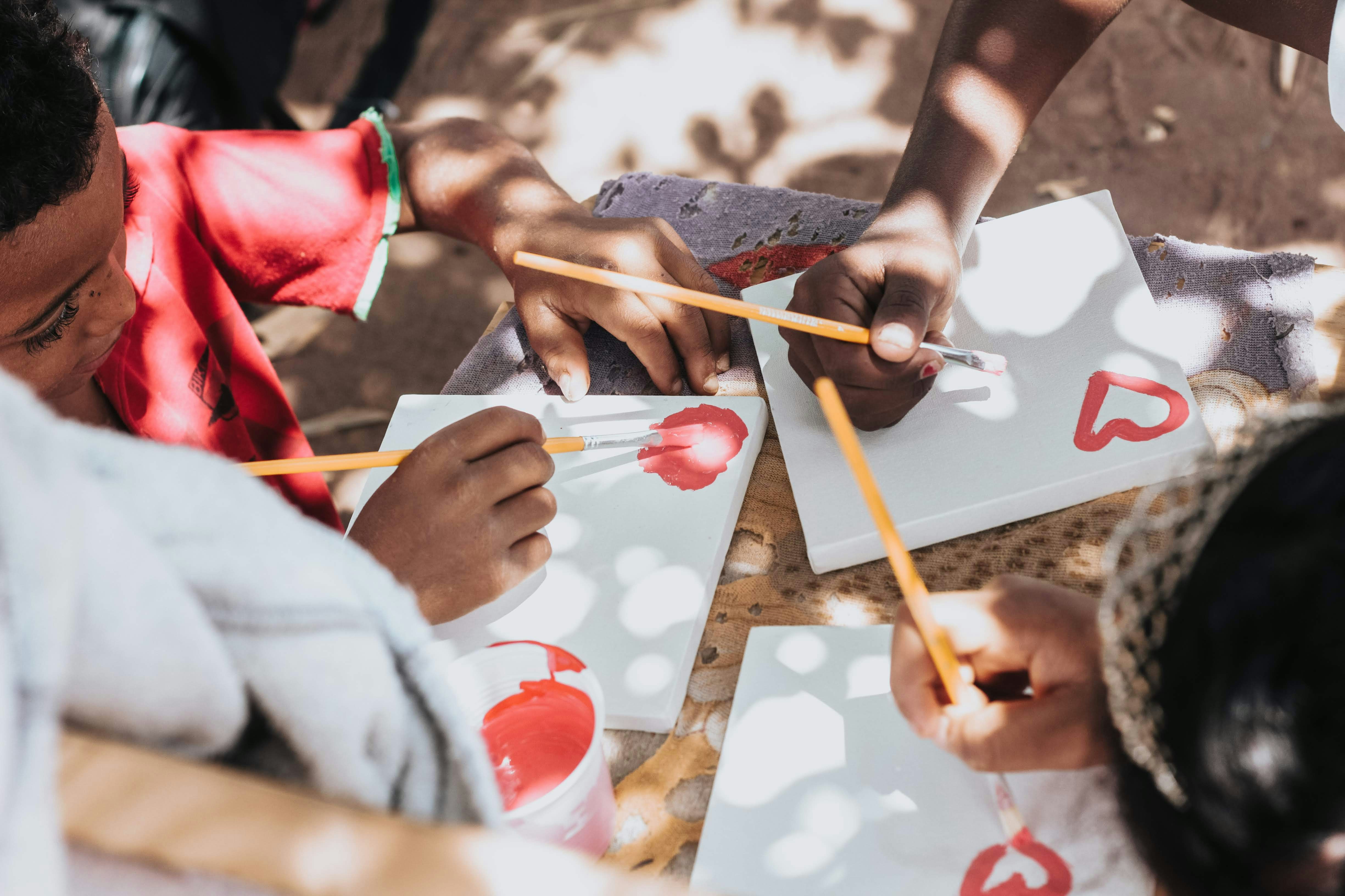 Children painting hearts on canvases outdoors