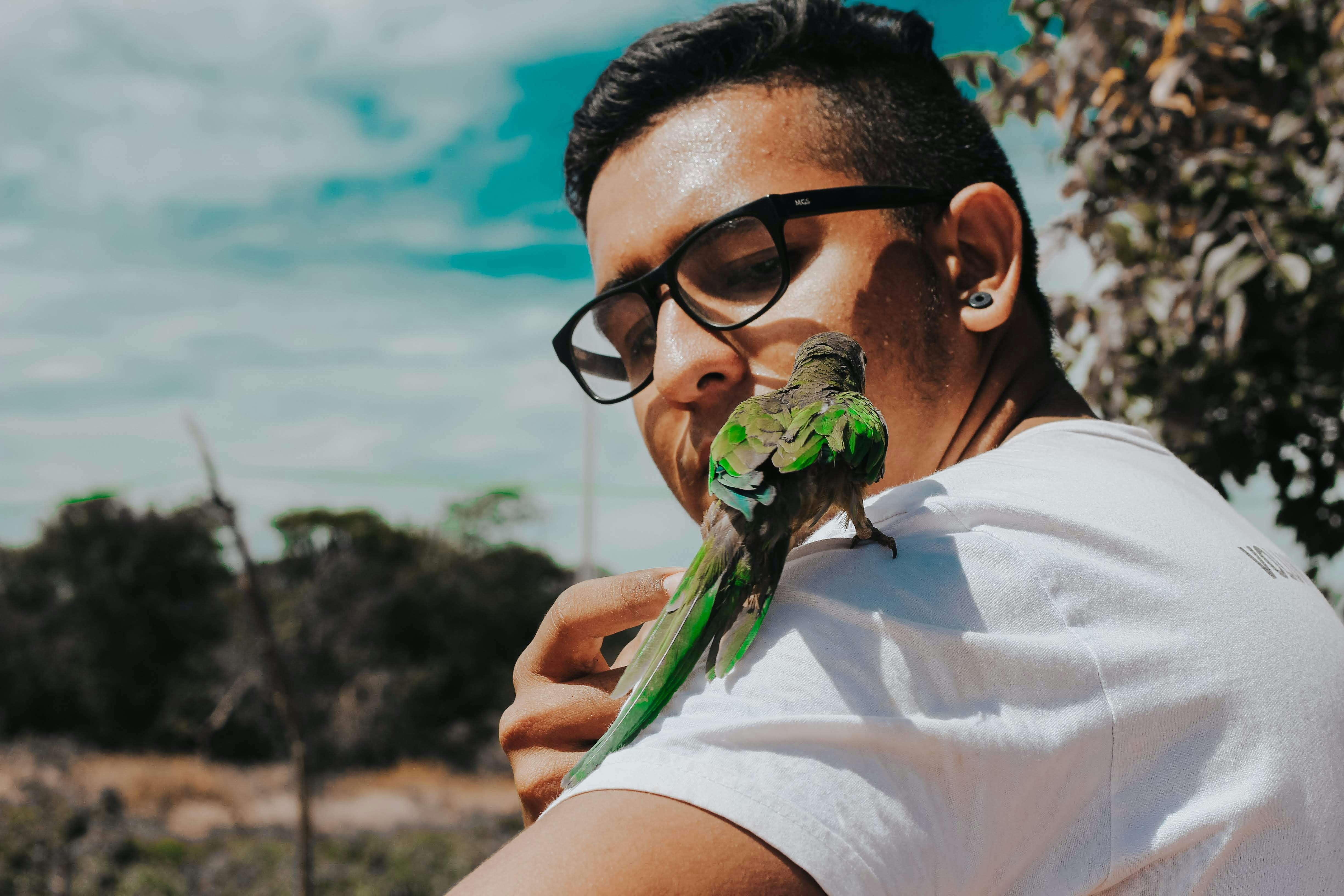 Man with glasses holding a green parrot on his shoulder