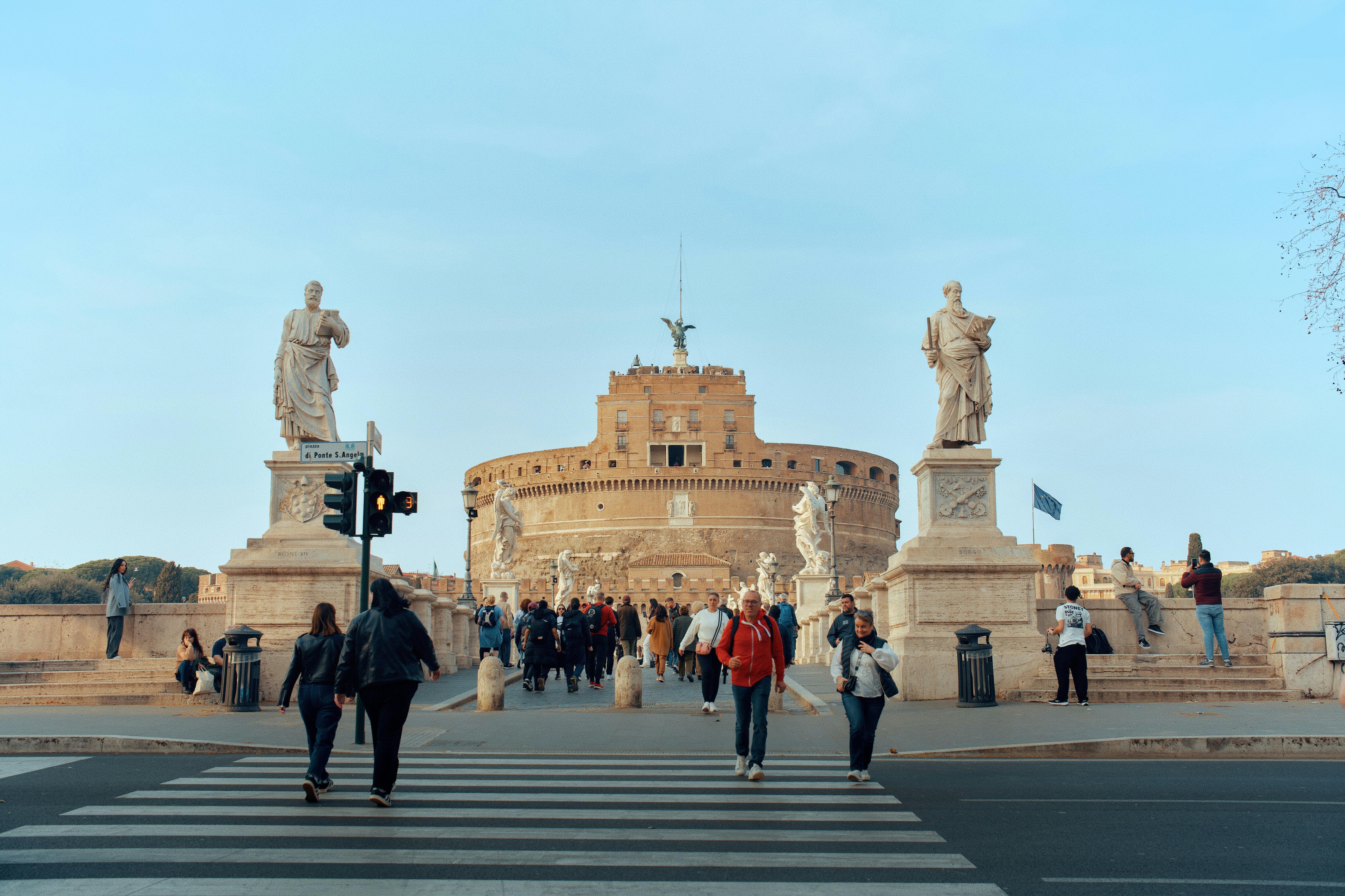 People walking towards a large circular building with statues.