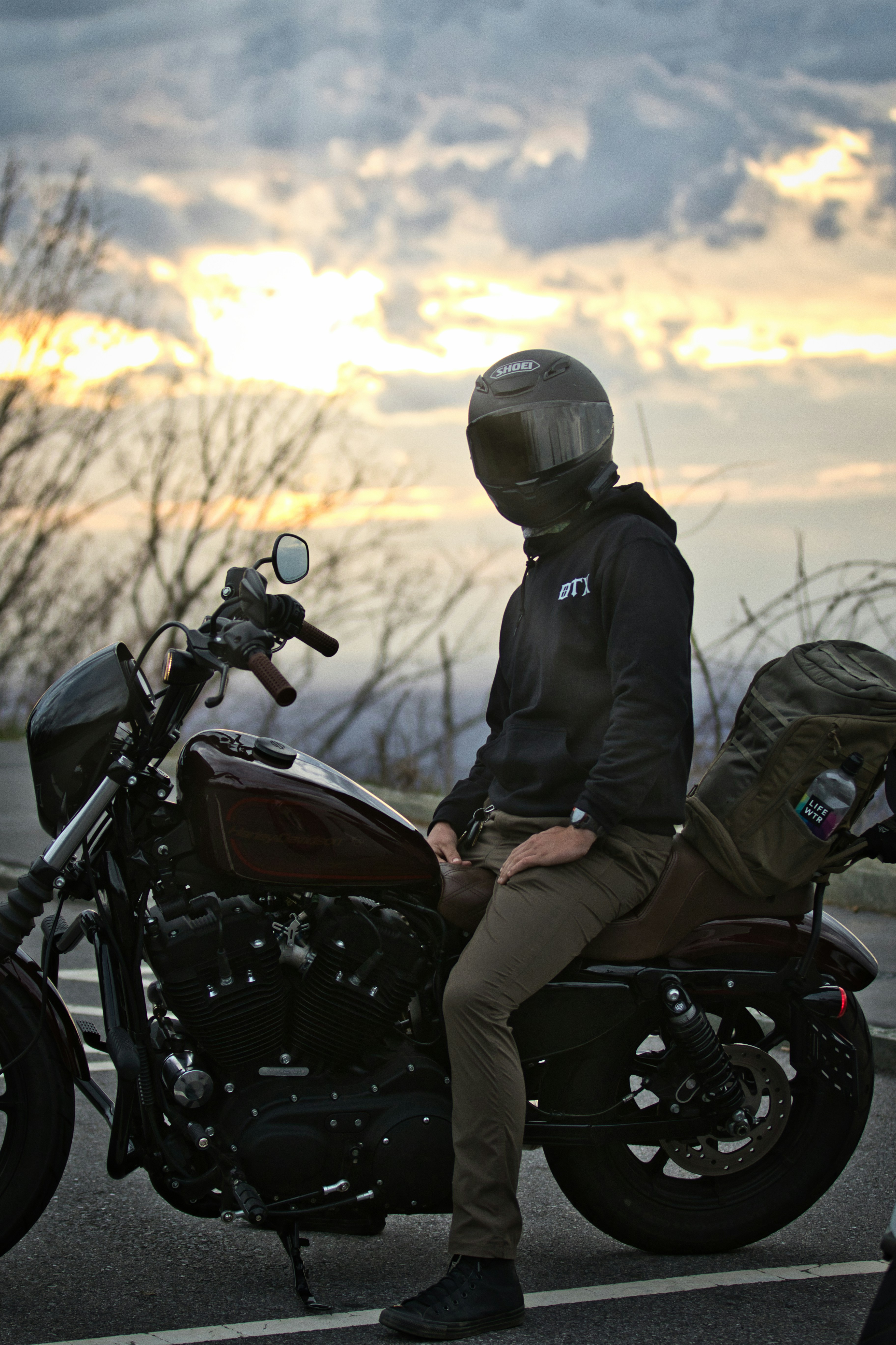 Personne casquée assise sur une moto au coucher du soleil