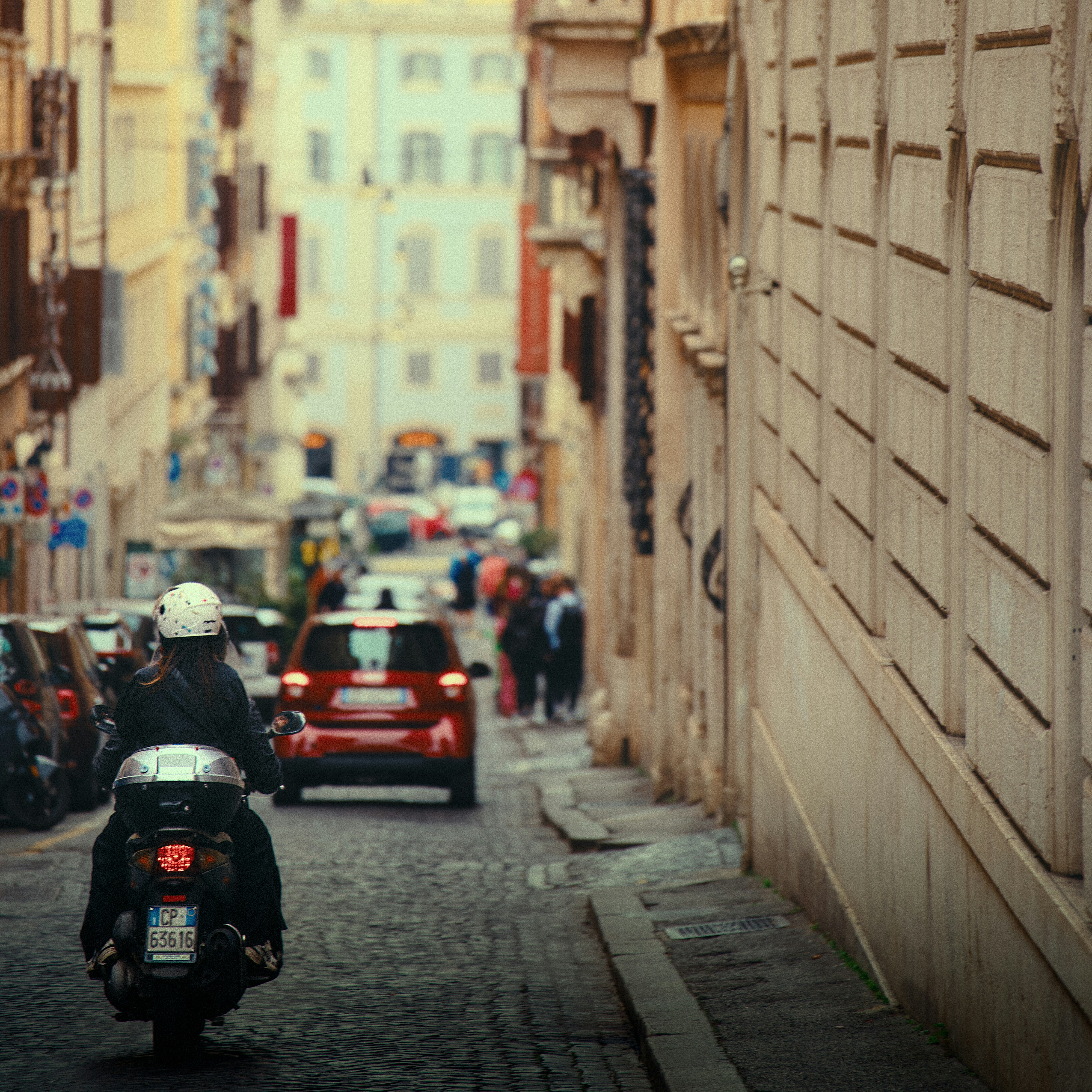 A scooter rides down a cobblestone street in rome.