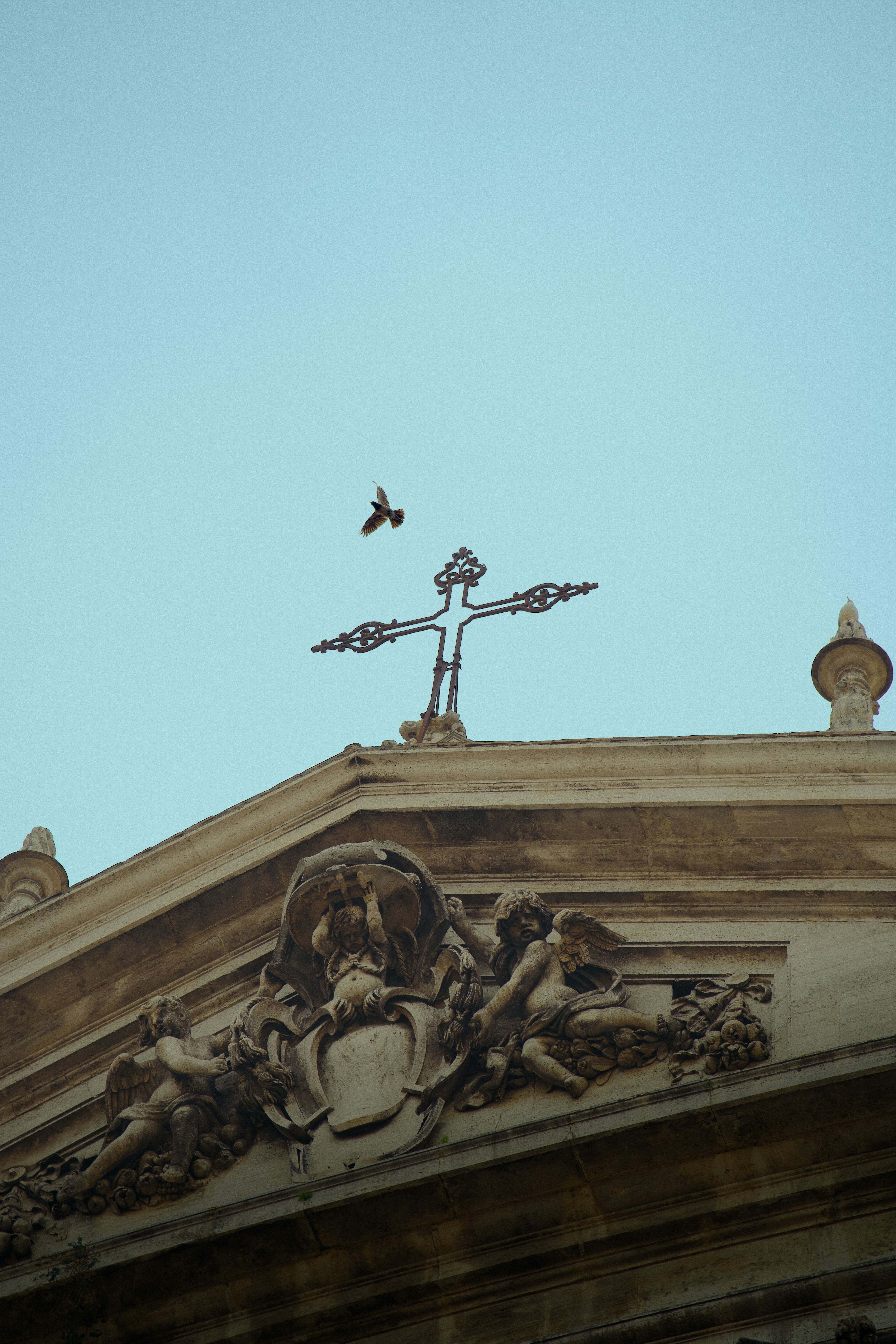 A cross adorns a building with a bird flying by