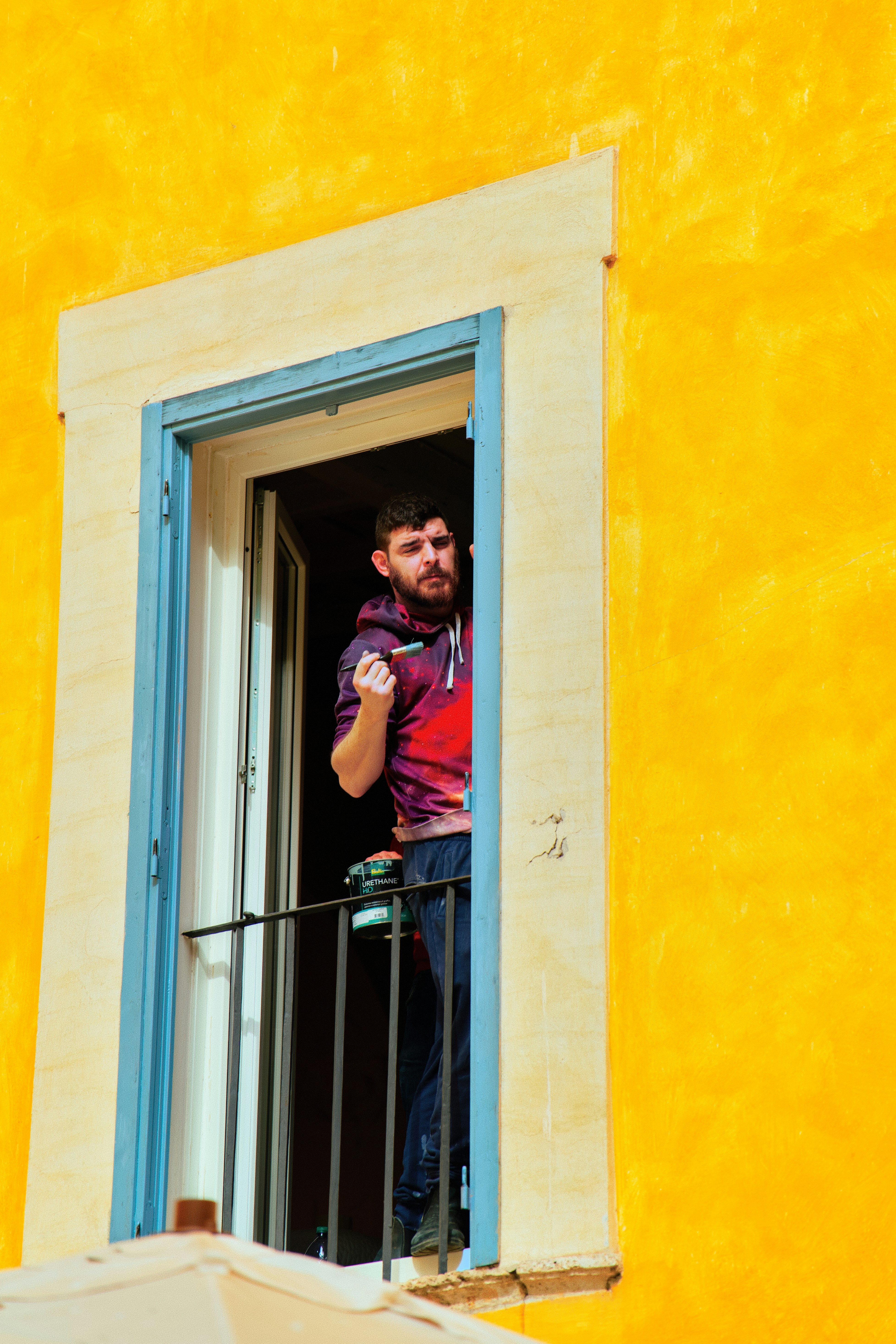 Man with beard looking out of a yellow window