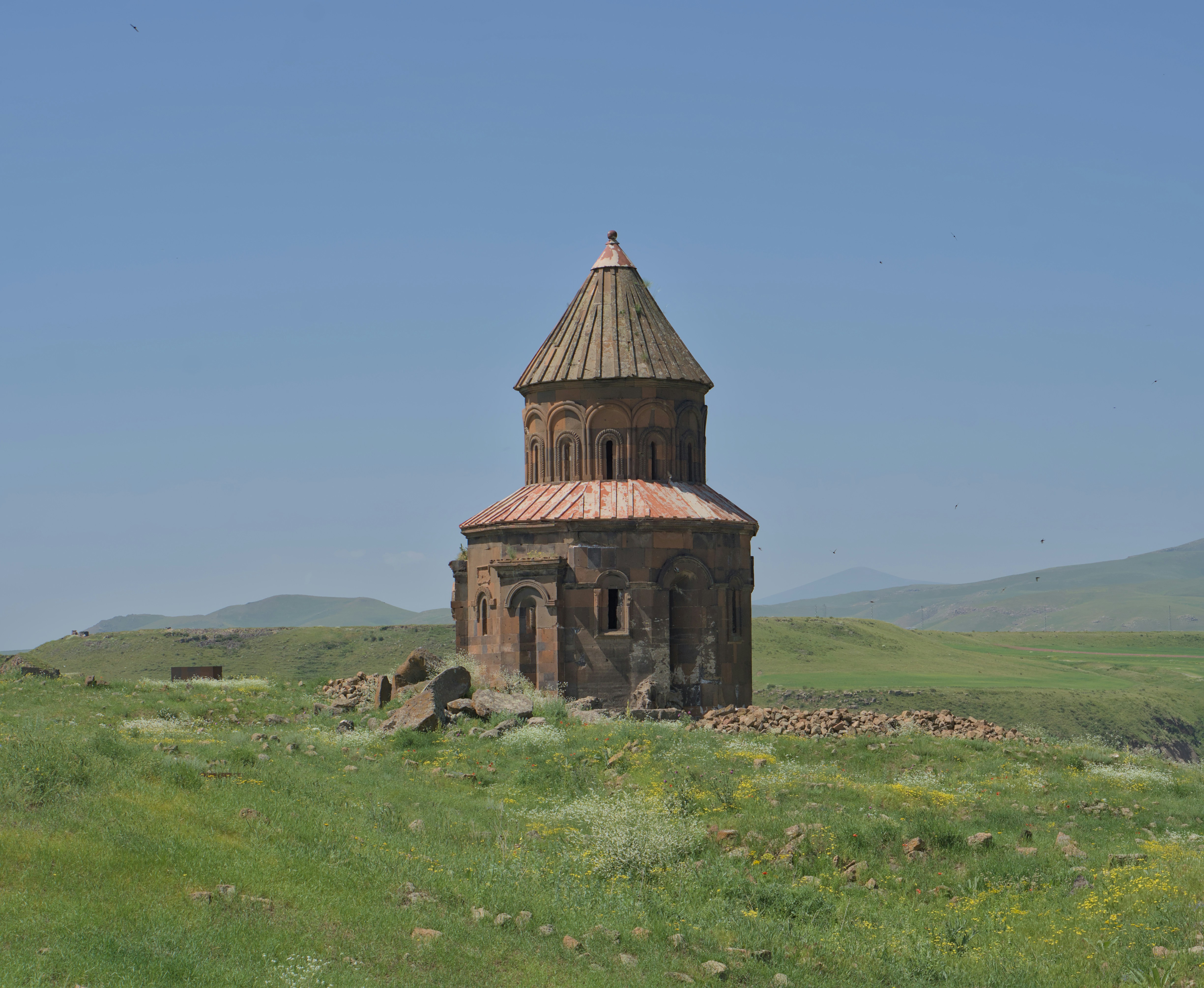 Antica chiesa in pietra su una collina erbosa sotto un cielo azzurro