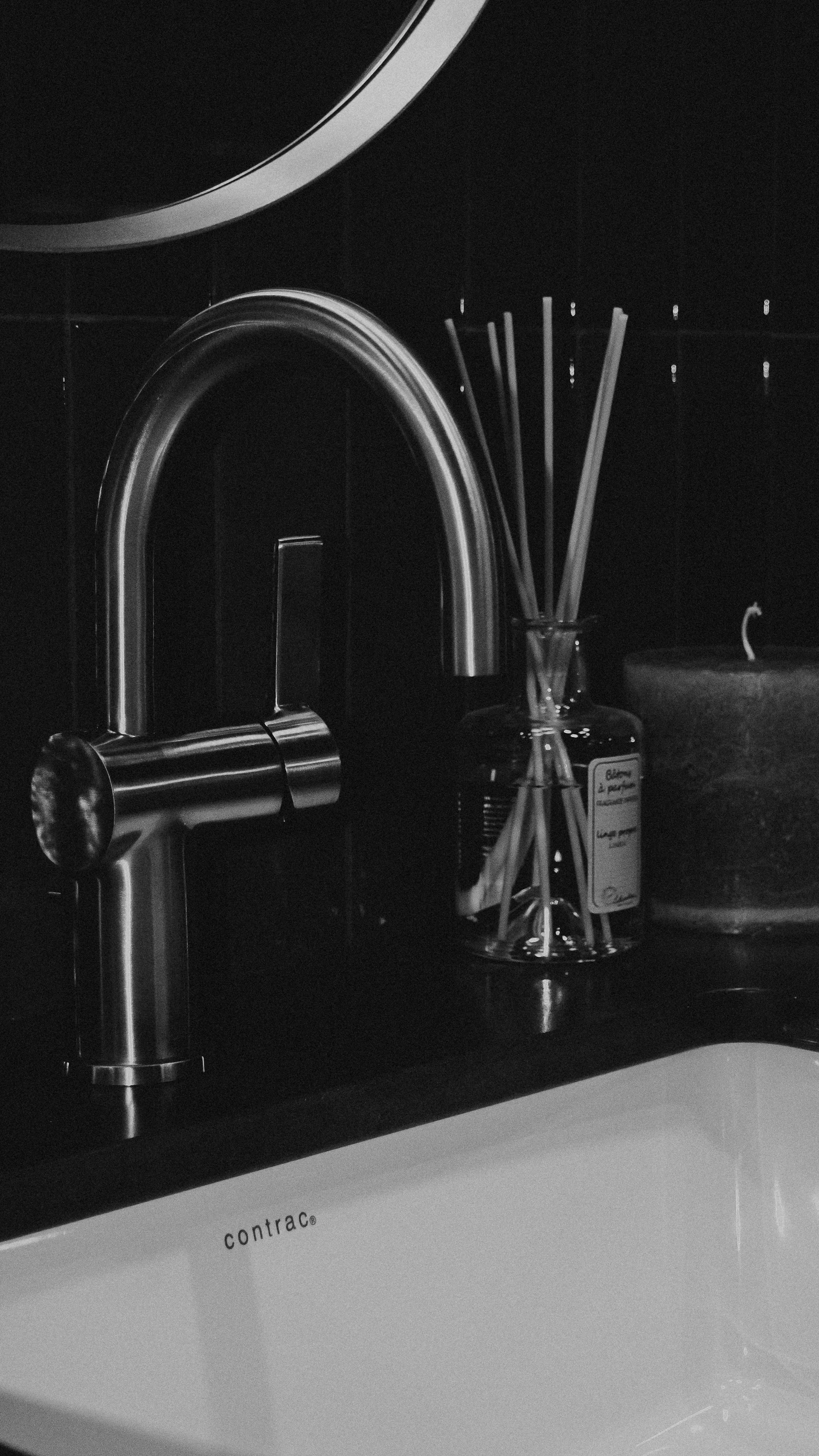 A modern sink faucet with reed diffuser and candle.