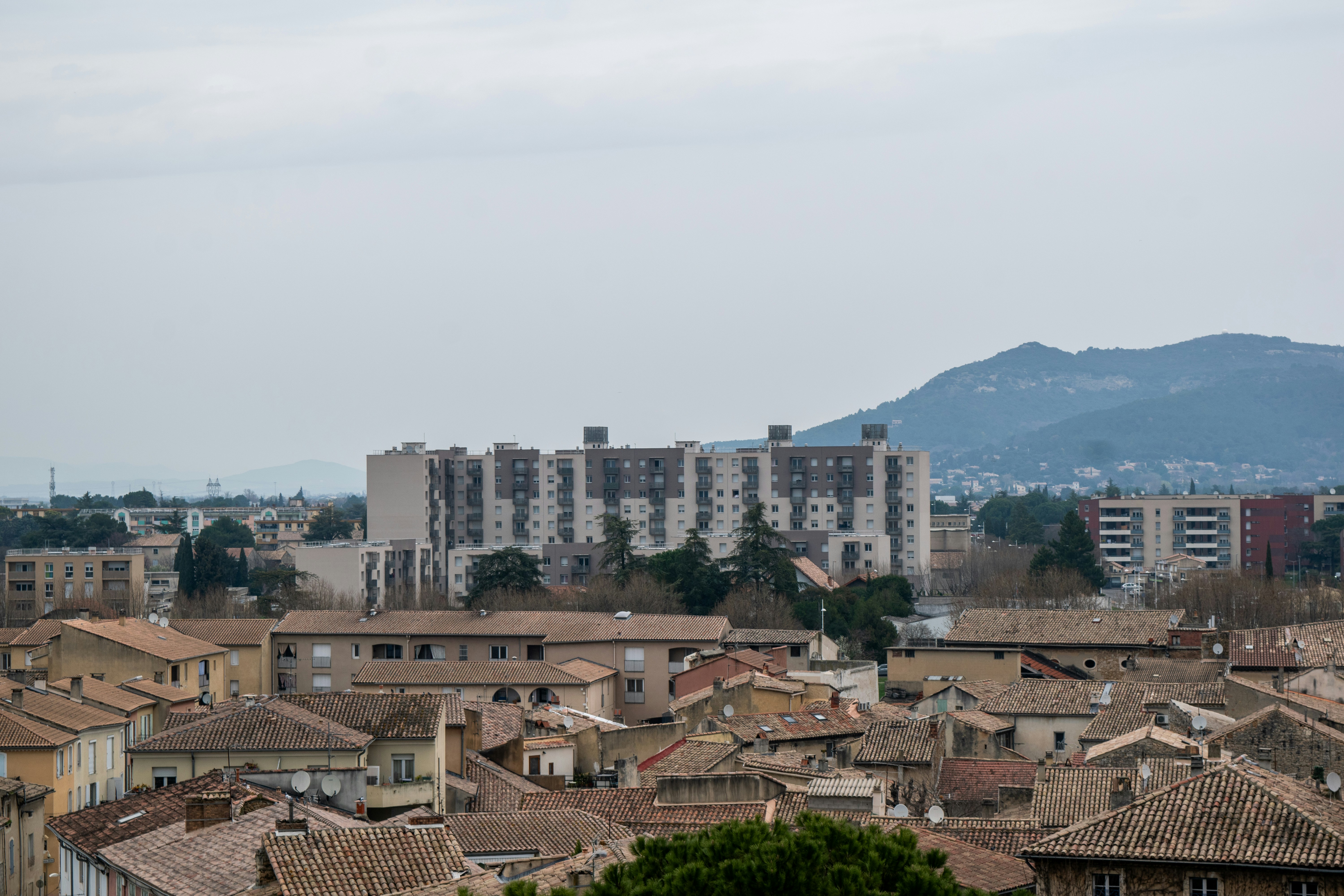 Apartment buildings rise above older rooftops with distant hills.