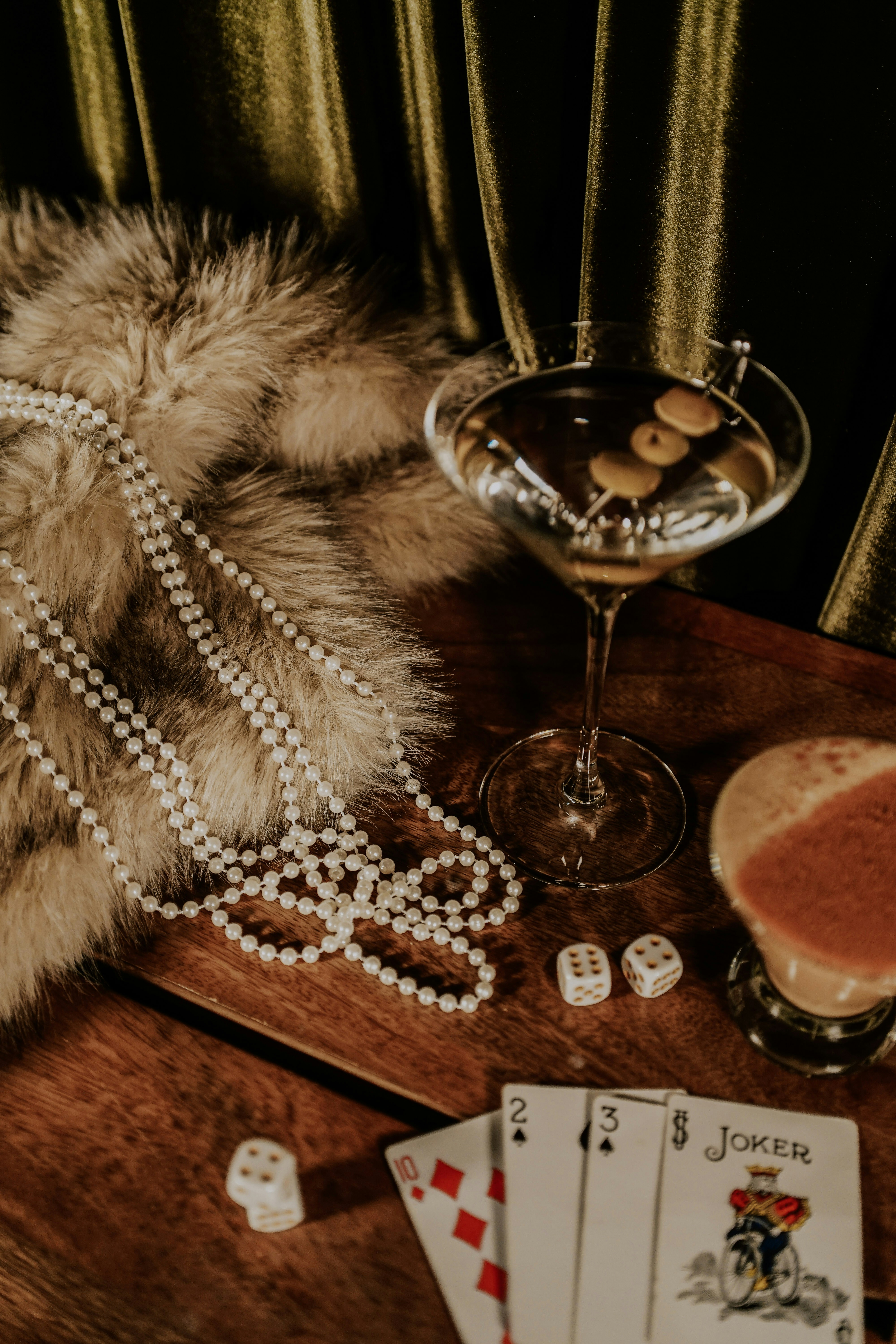 Martini, pearls, dice, and playing cards on a table.