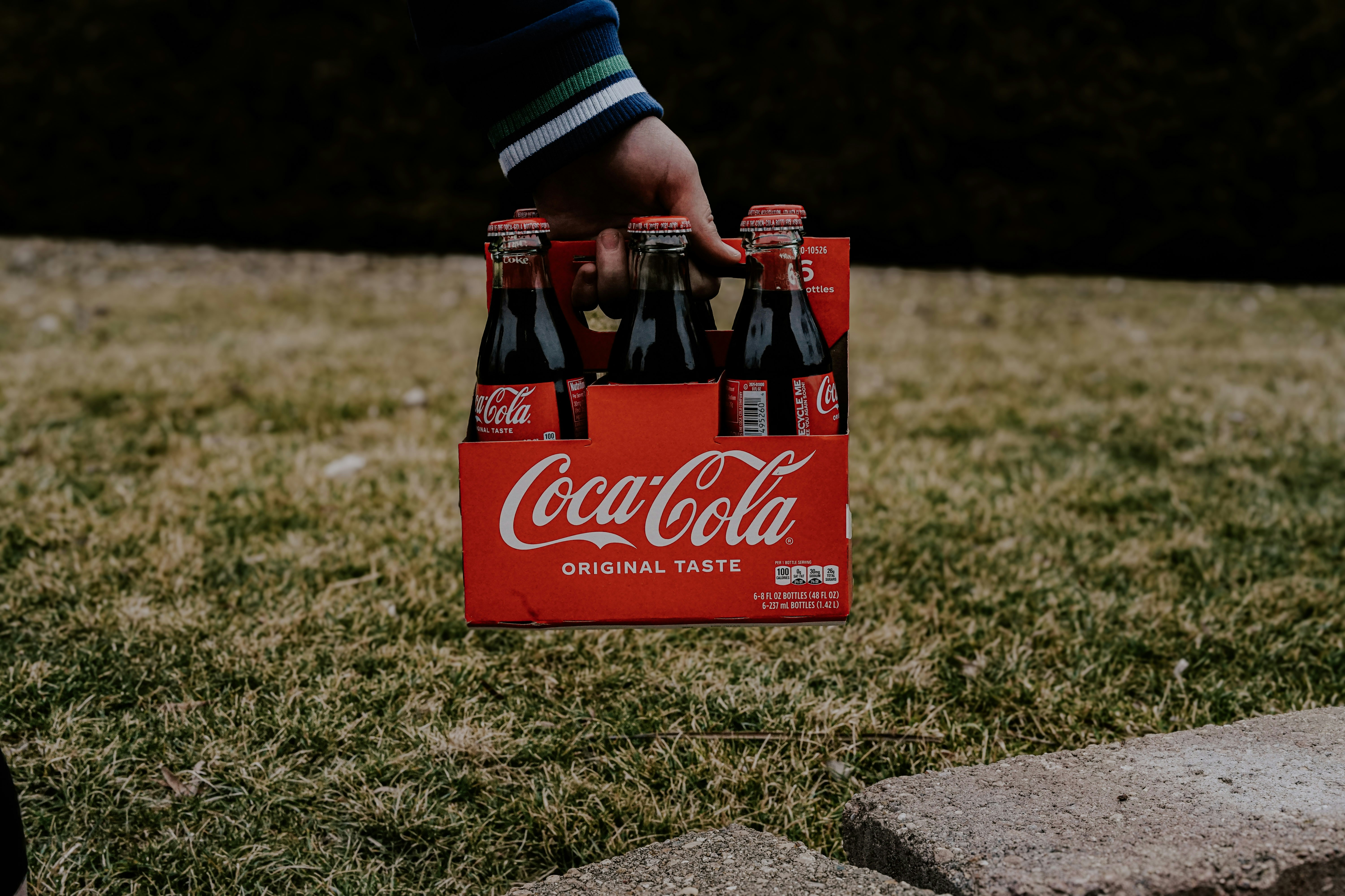 Hand holding a six-pack of coca-cola bottles outdoors