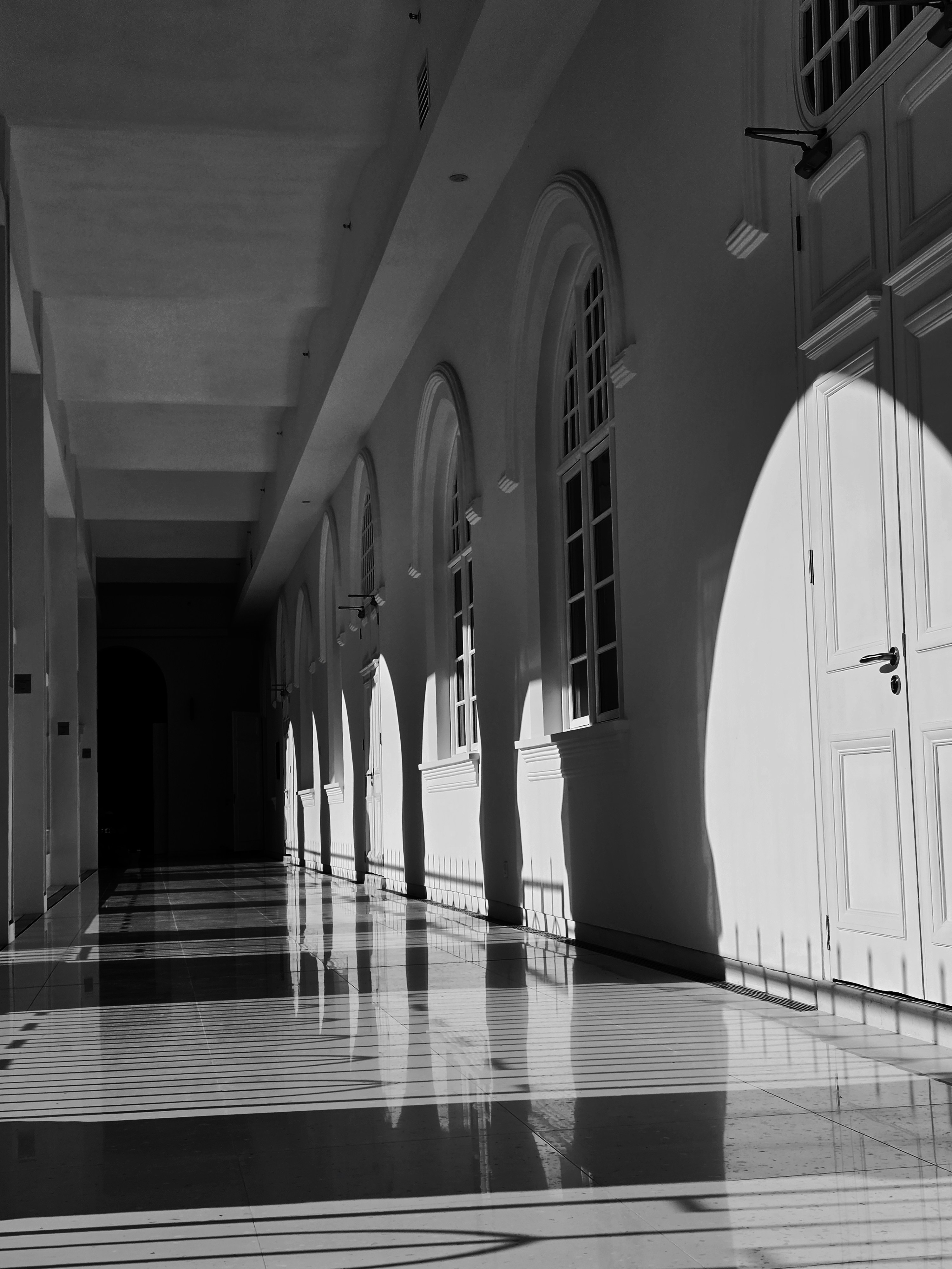 Sunlight streams into a long, empty hallway with arched windows.