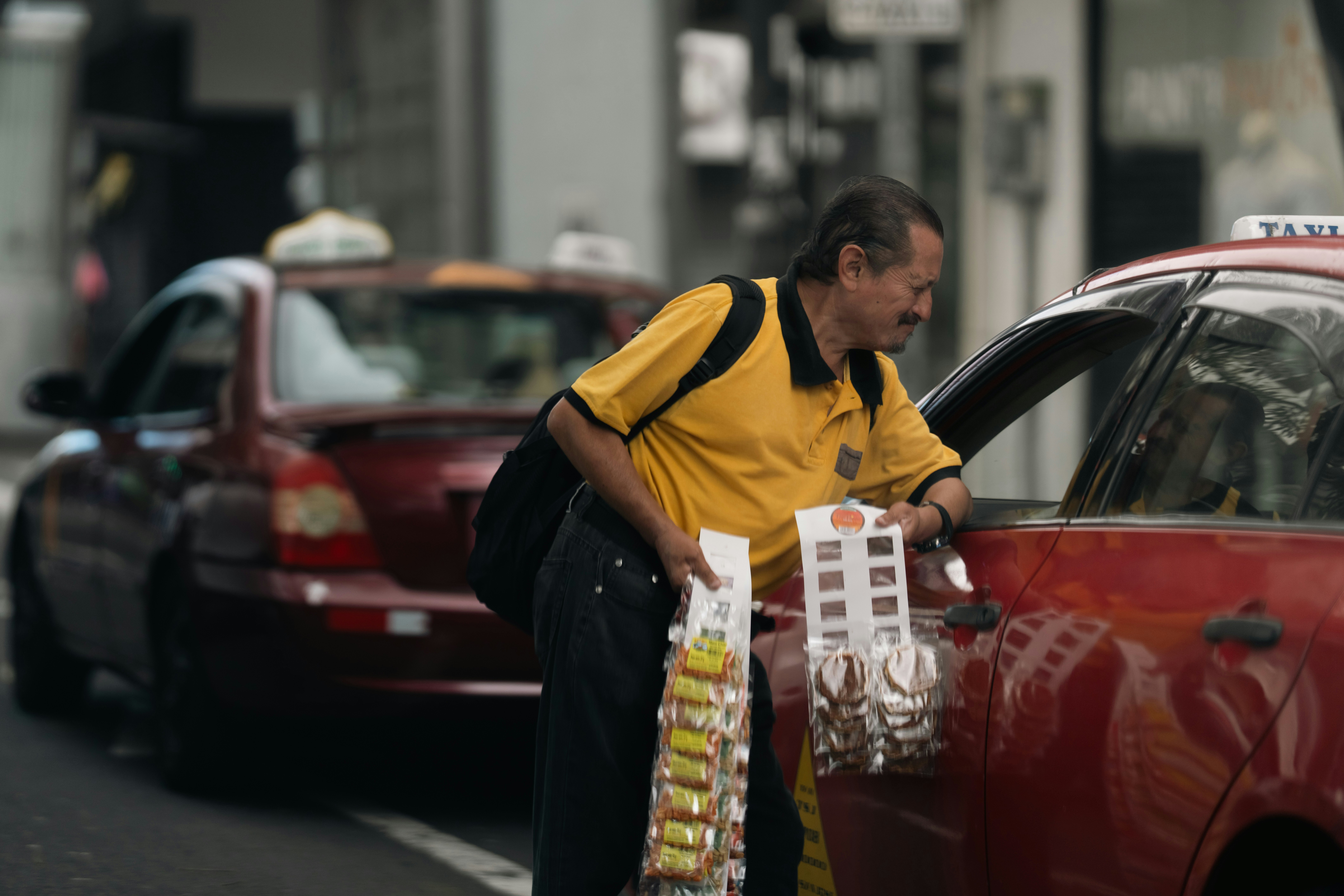 Man selling goods next to a red taxi.