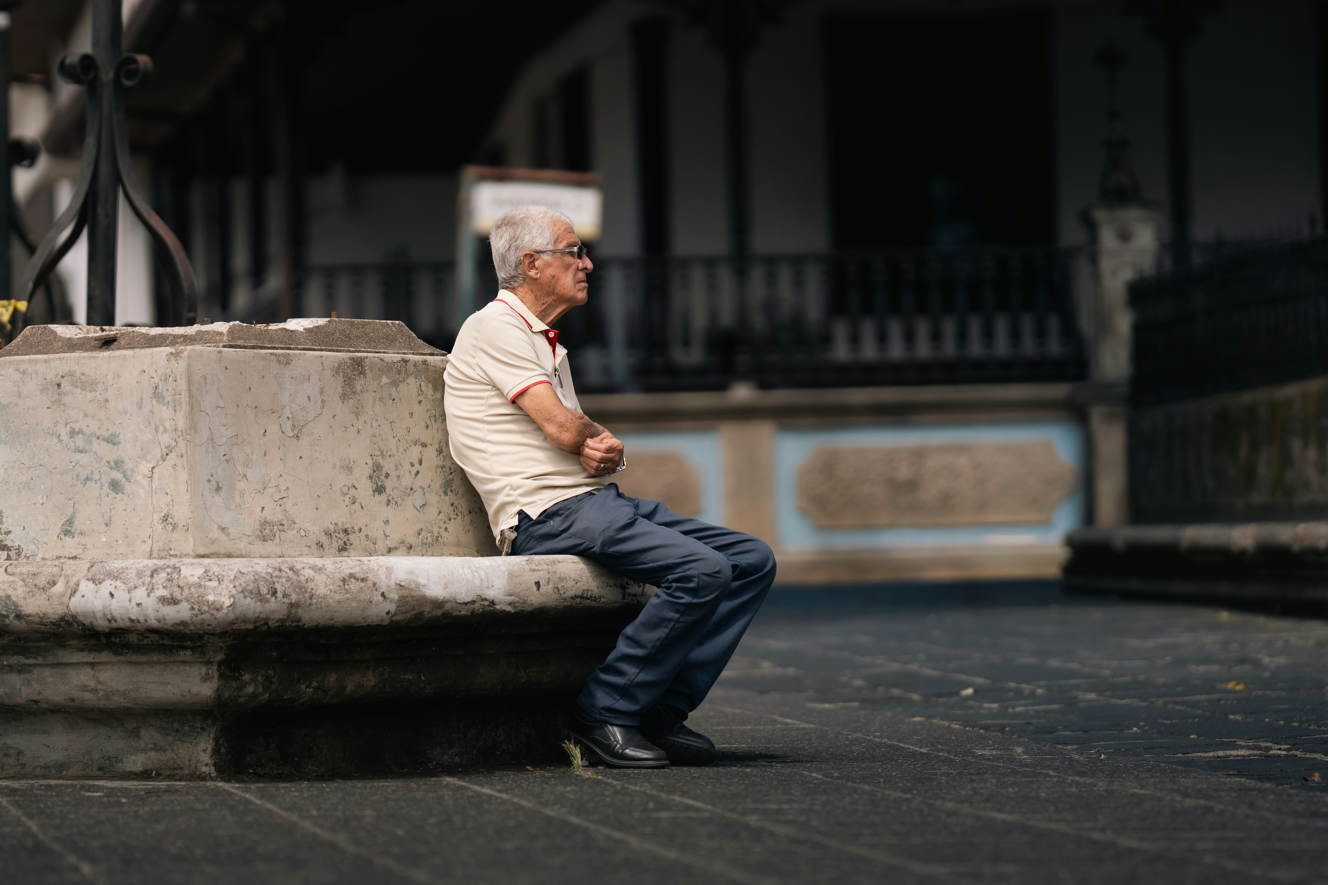 Elderly man sitting on a stone bench outdoors.