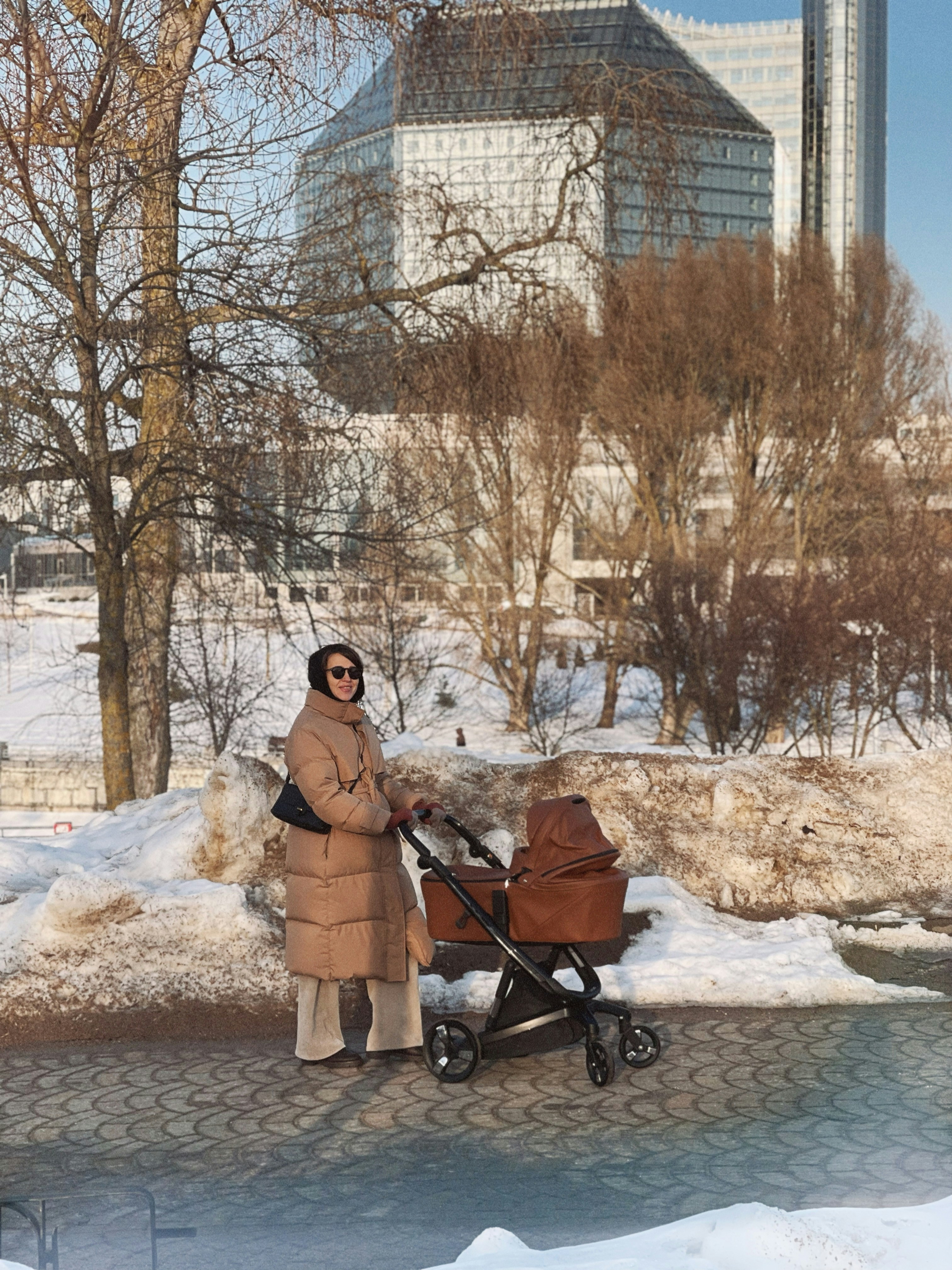 Frau mit Kinderwagen im verschneiten Park mit modernem Gebäude